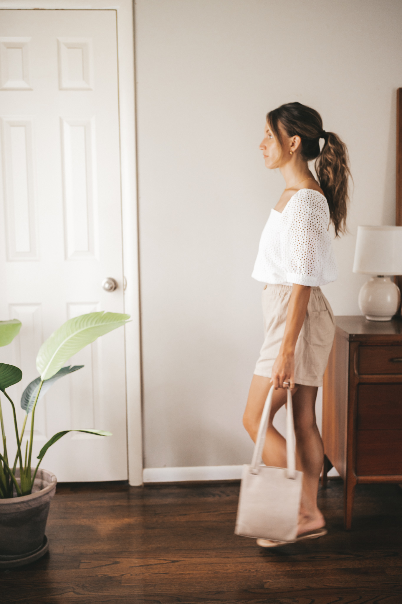 ashley wearing a white puff sleeve eyelet top, tan linen blend shorts, nude sandals, and a gray shoulder bag
