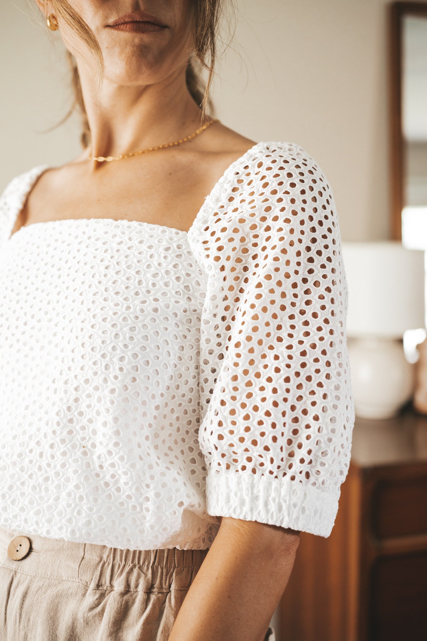 ashley wearing a white puff sleeve eyelet top, tan linen blend shorts, nude sandals, and a gray shoulder bag
