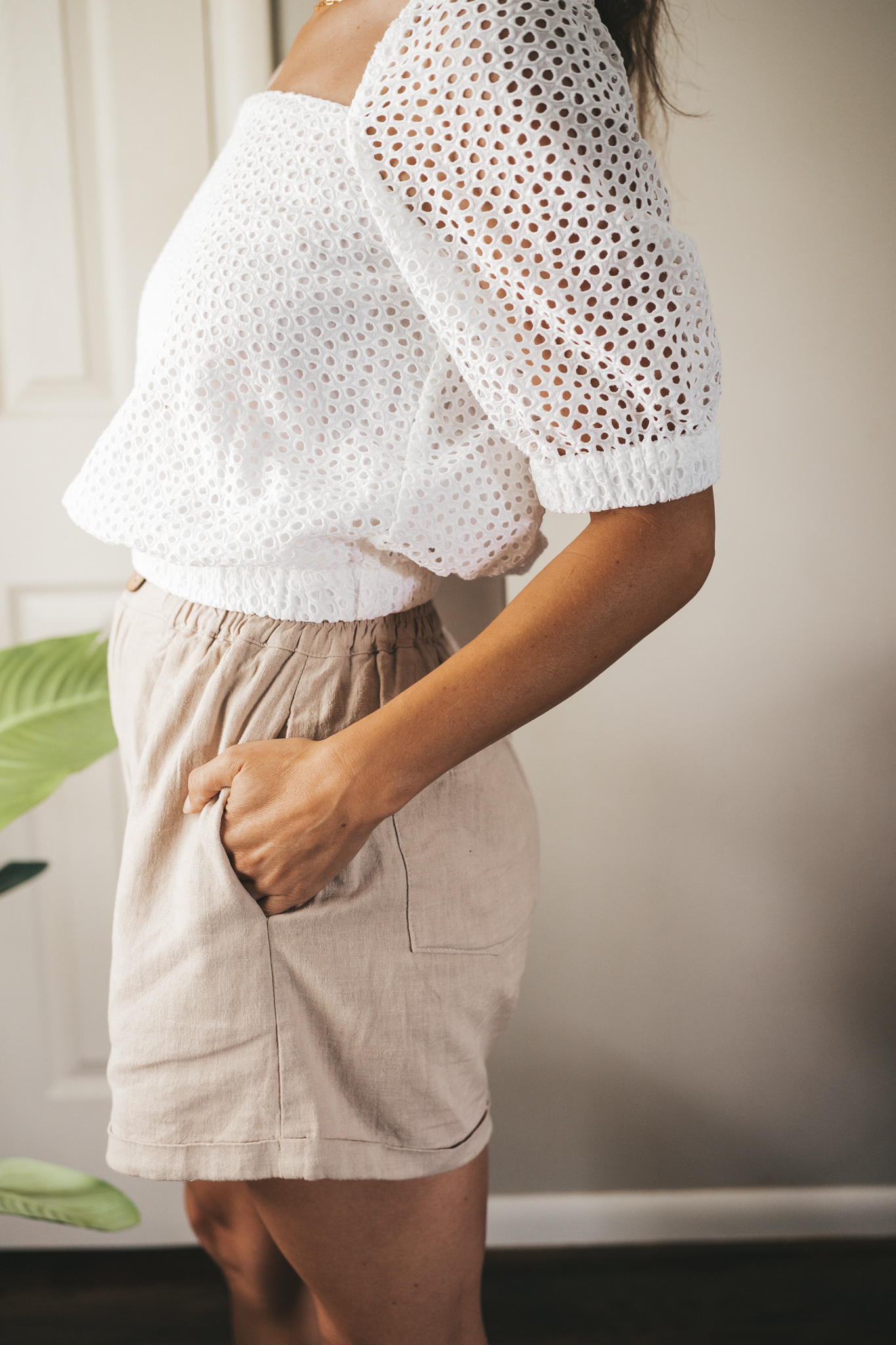 ashley wearing a white puff sleeve eyelet top, tan linen blend shorts, nude sandals, and a gray shoulder bag