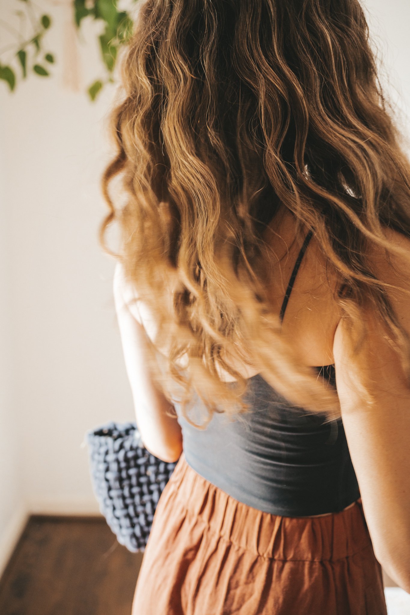 ashley wearing a cropped black tank, dark orange midi skirt with buttons down the front, black strappy sandals, a gold pendant necklace, and a black woven bag