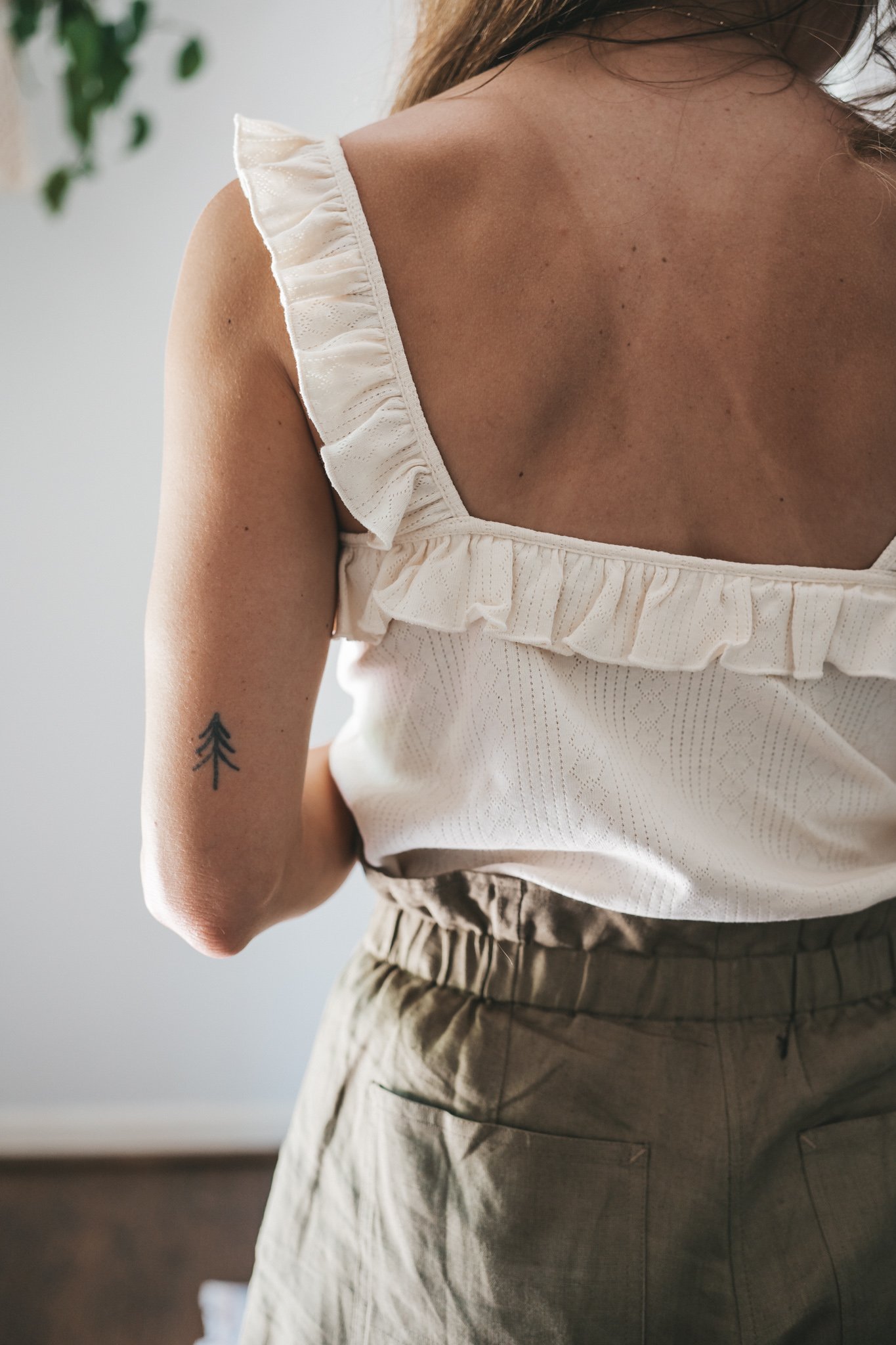 ashley wearing a cream colored tank with ruffled sleeves, olive green paperbag shorts, brown leather sandals, and a woven bag