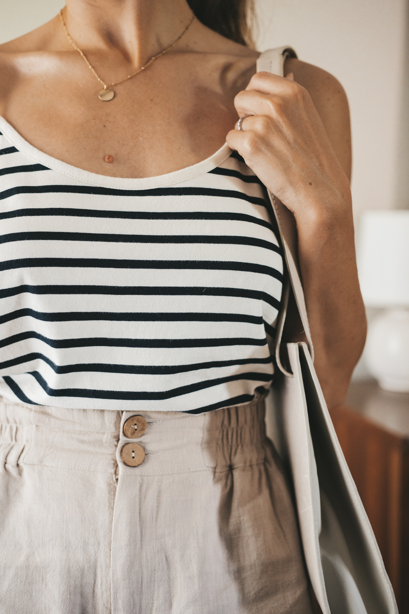 ashley wearing a white and navy striped tank, tan linen shorts, white sandals, a gray shoulder bag, and tortoise shell sunglasses