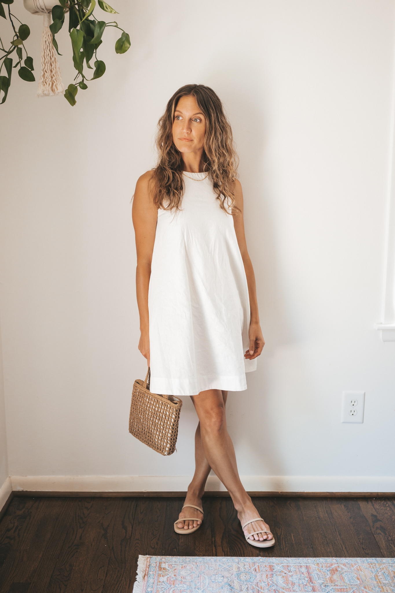 ashley wearing a white linen shift dress, nude sandals, and a woven bag