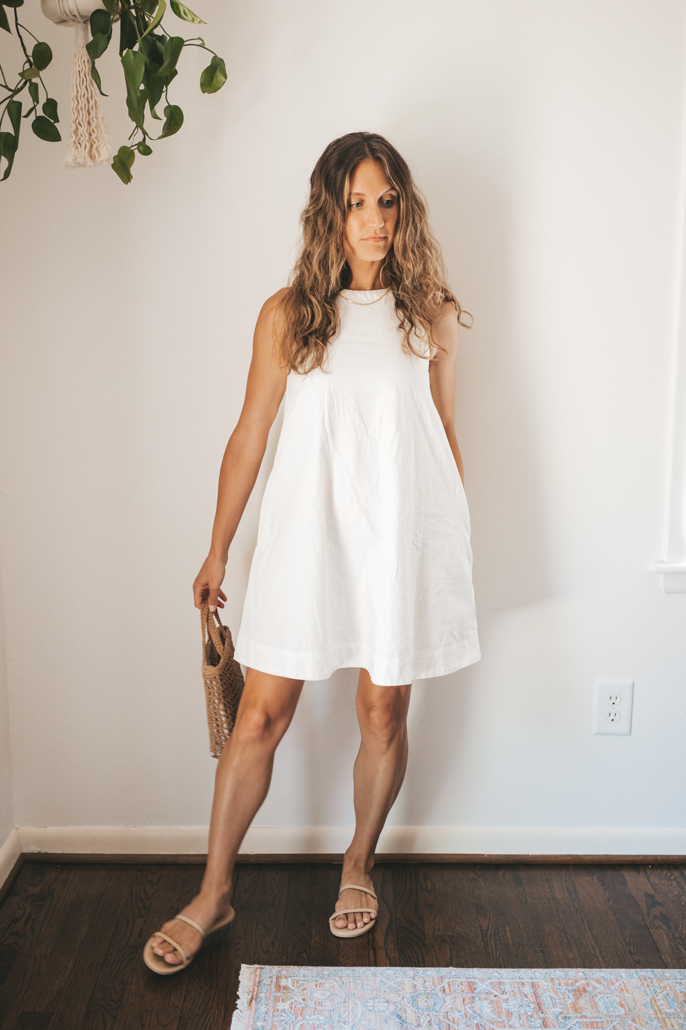 ashley wearing a white linen shift dress, nude sandals, and a woven bag
