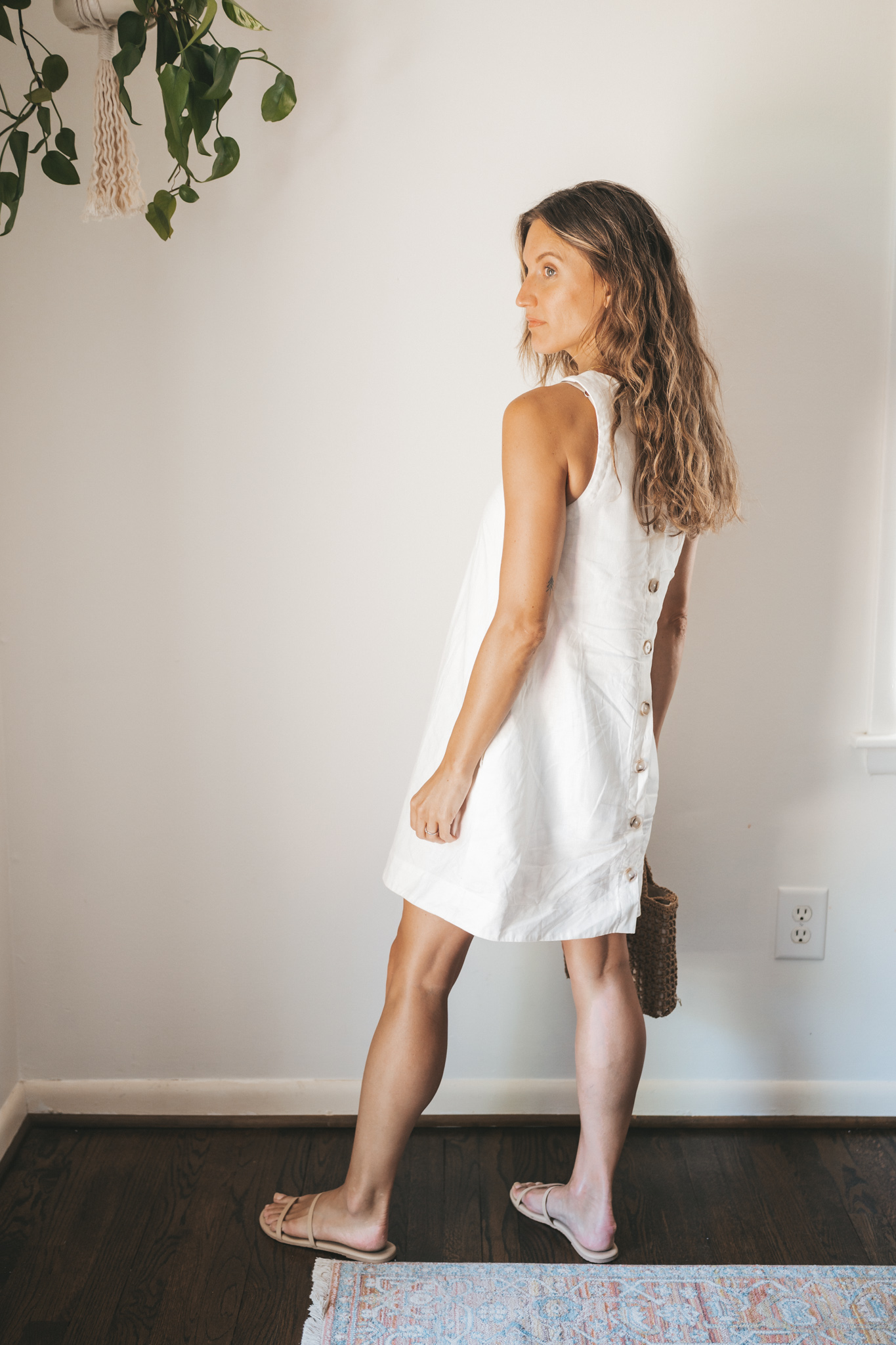 ashley wearing a white linen shift dress, nude sandals, and a woven bag