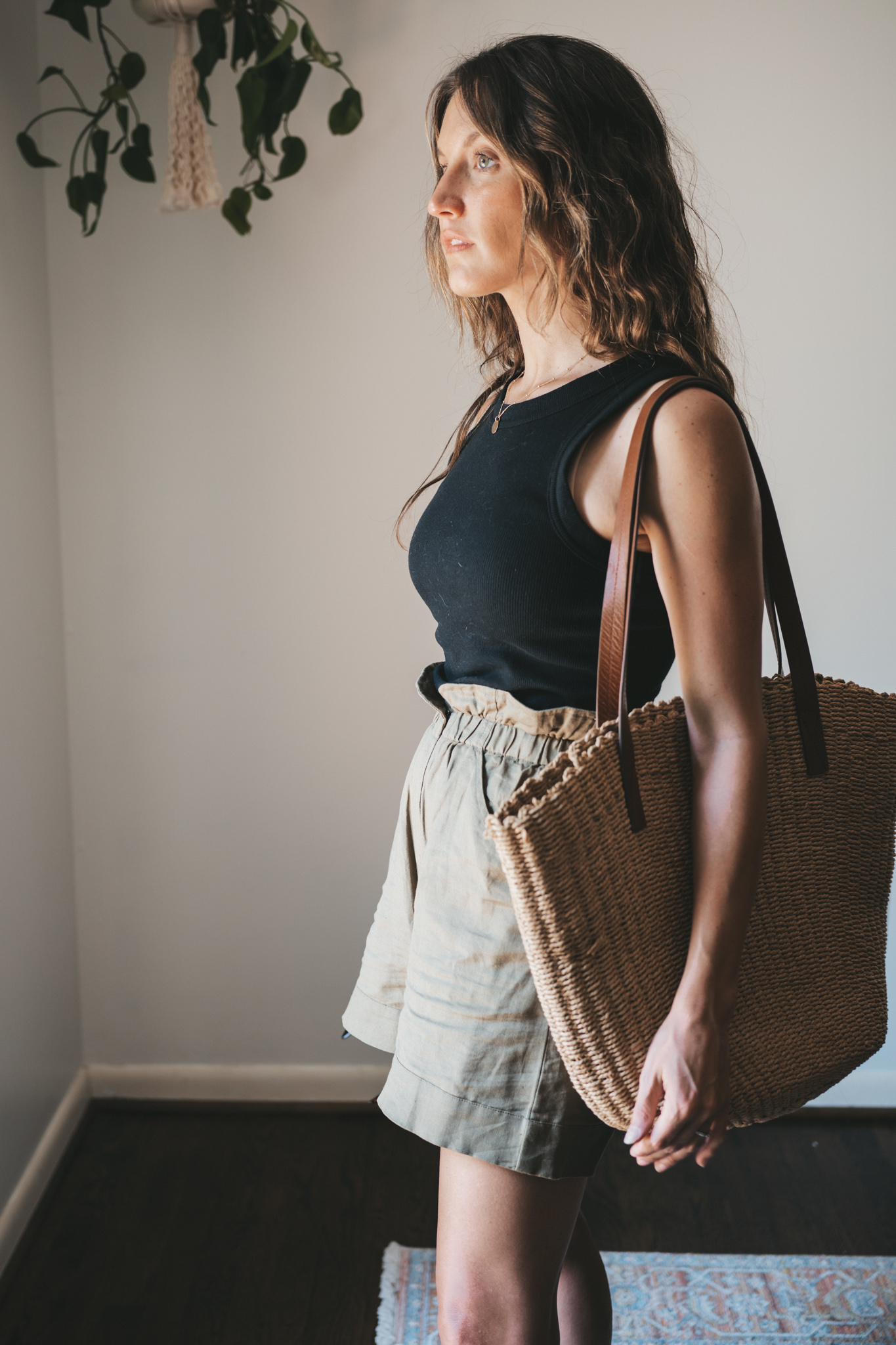 ashley wearing a black ribbed tank, green paperbag shorts, brown leather toe ring sandals, a woven tote bag, and tortoise shell sunglasses