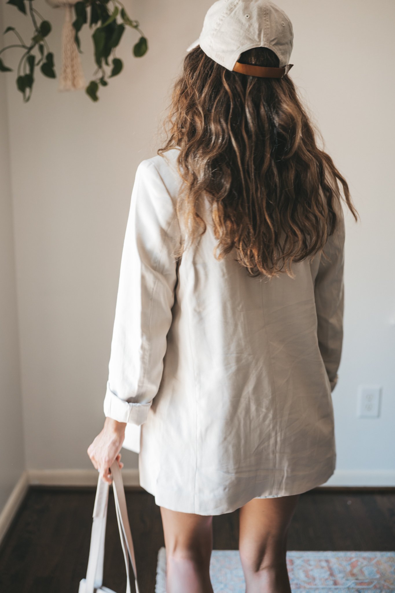 ashley wearing a white tee, beige oversized blazer, light wash long length denim shorts, white sneakers and a beige baseball cap with a gray shoulder bag