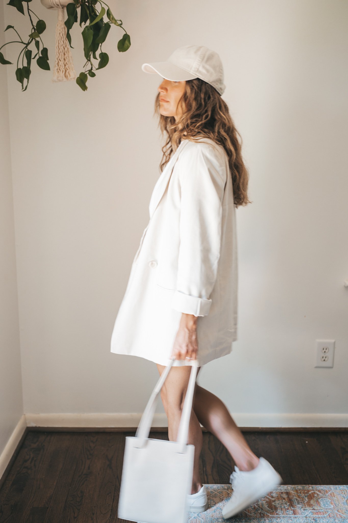 ashley wearing a white tee, beige oversized blazer, light wash long length denim shorts, white sneakers and a beige baseball cap with a gray shoulder bag