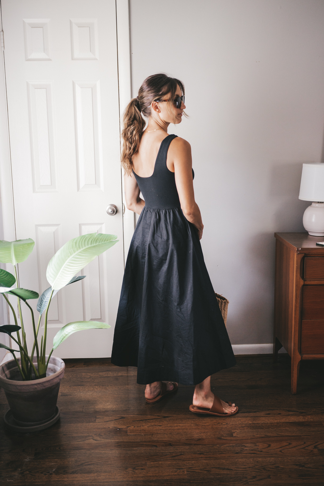 ashley wearing a black A-Line dress, brown leather sandals and a tan woven tote bag