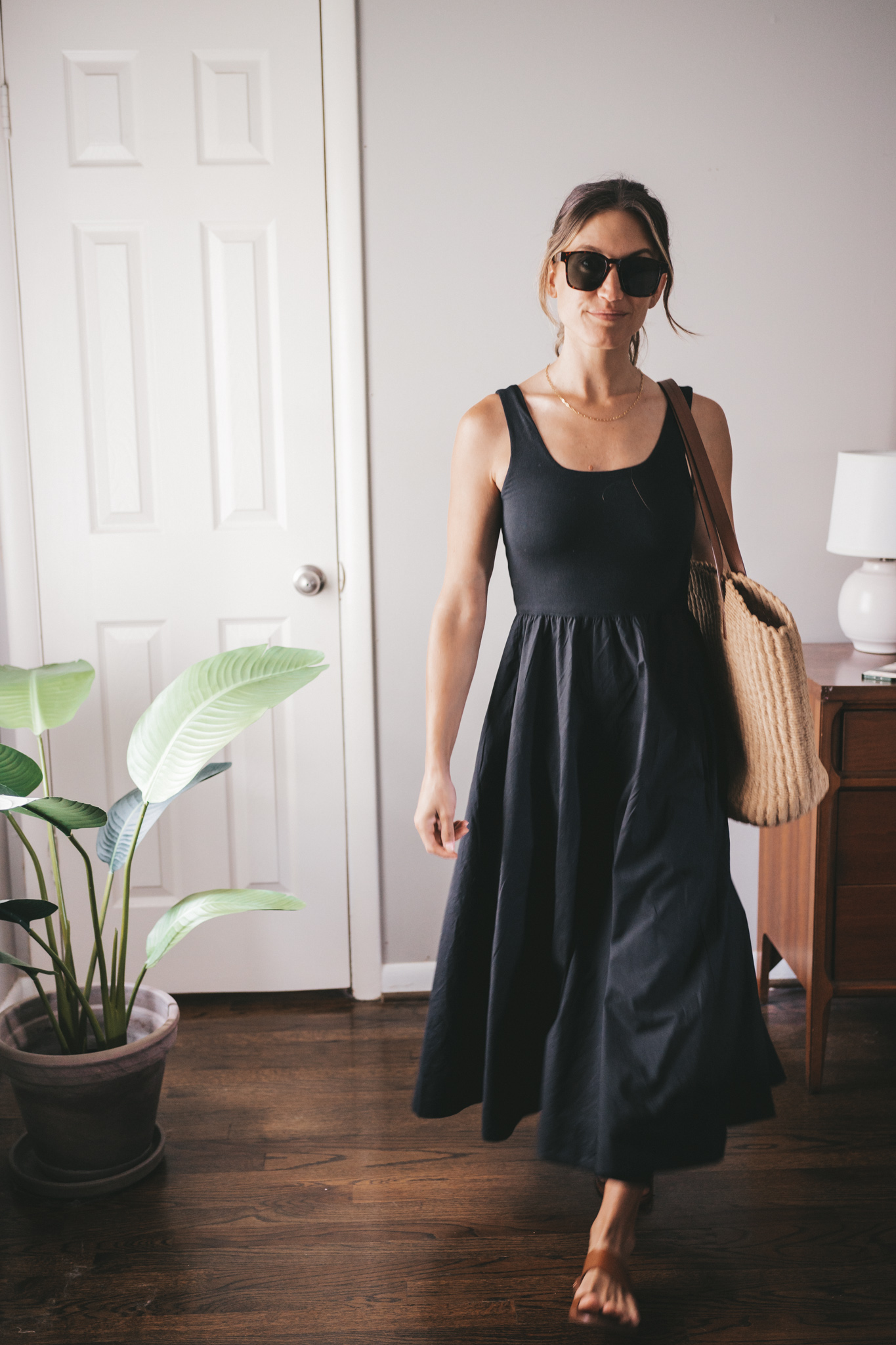 ashley wearing a black A-Line dress, brown leather sandals and a tan woven tote bag