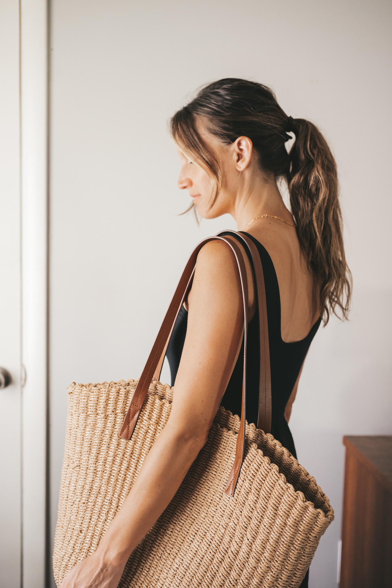 ashley wearing a black A-Line dress, brown leather sandals and a tan woven tote bag