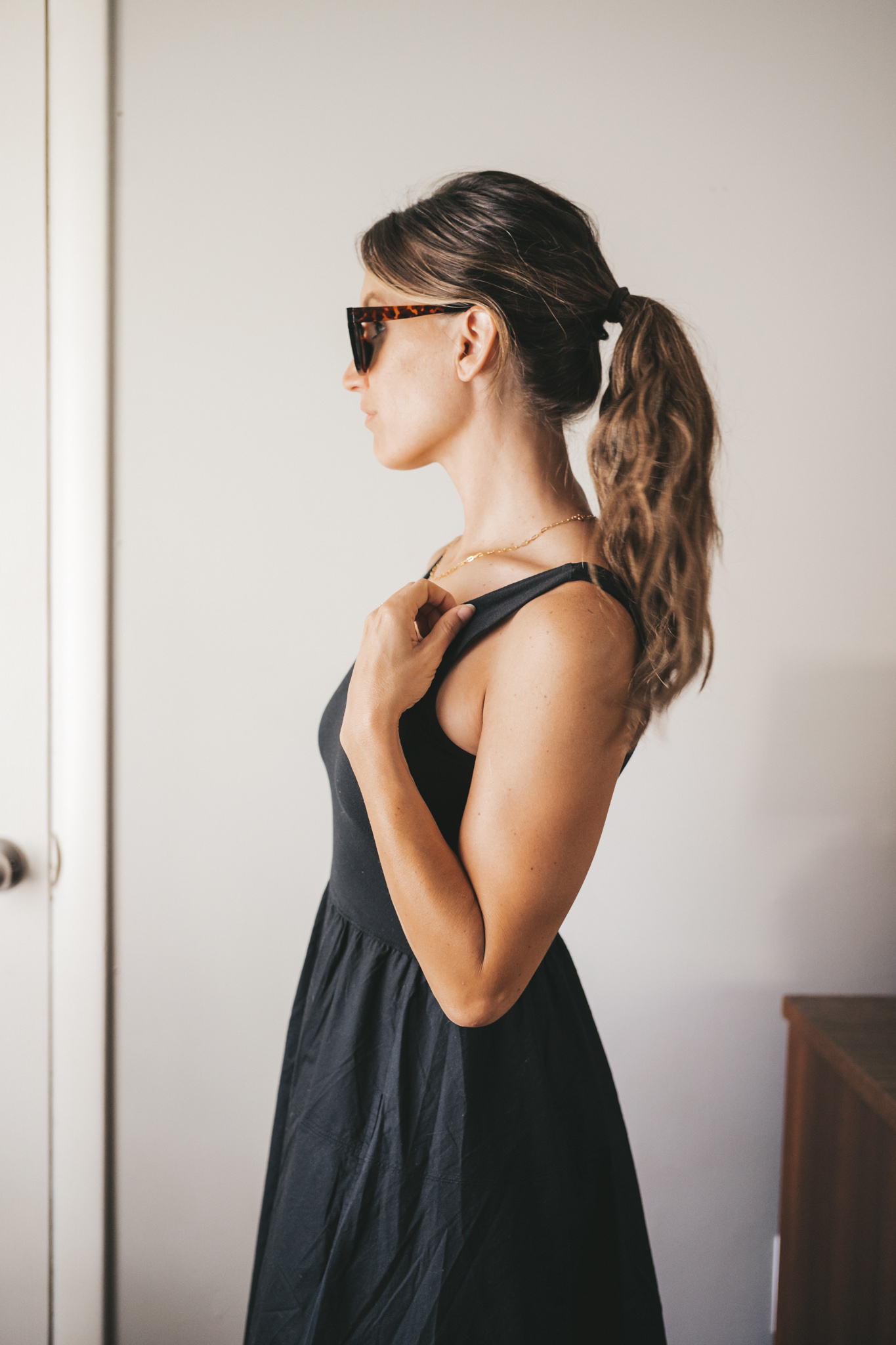 ashley wearing a black A-Line dress, brown leather sandals and a tan woven tote bag