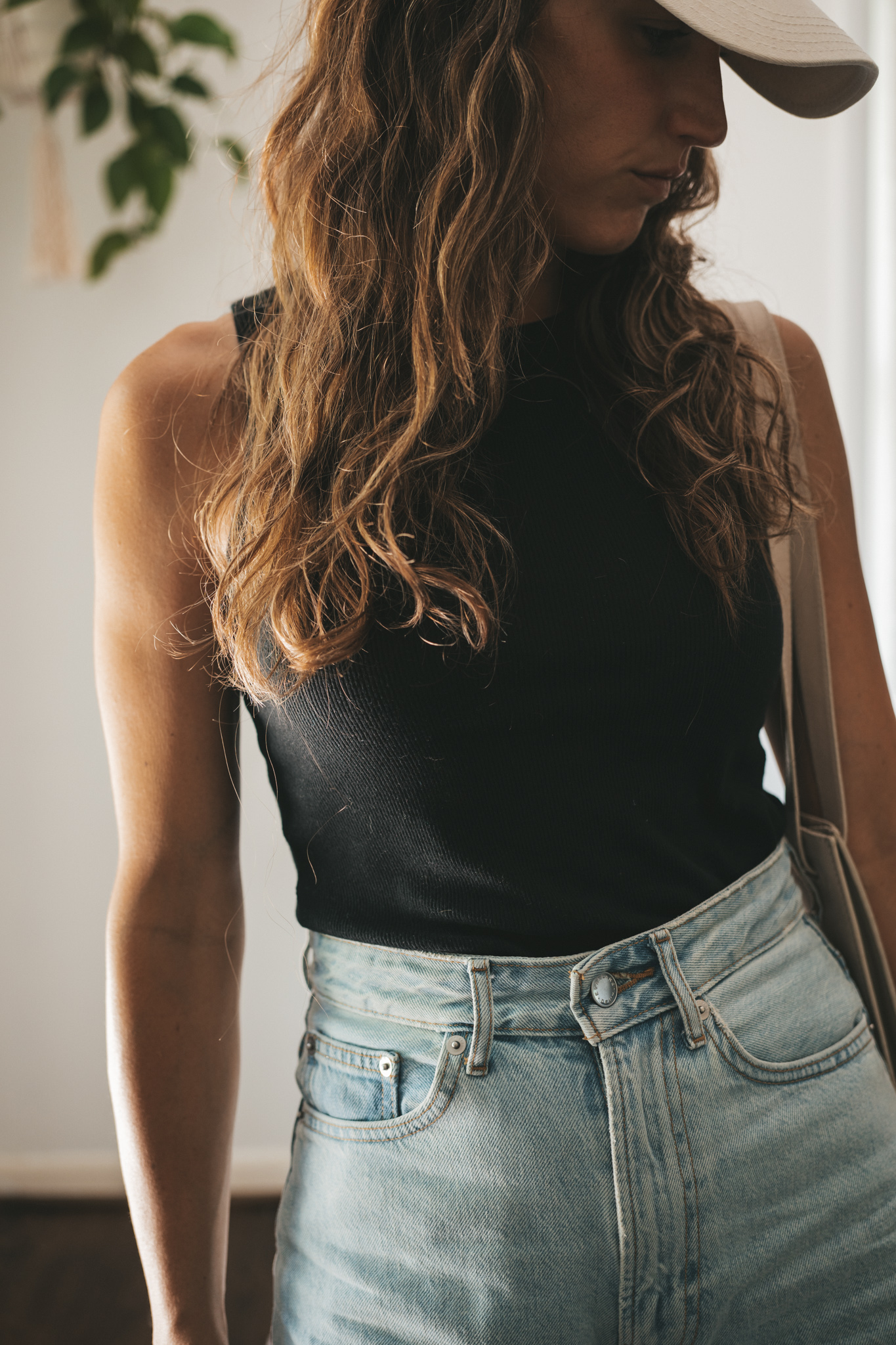 ashley wearing a black ribbed tank, light wash denim shorts, white sneakers, a beige baseball cap, and a gray leather shoulder bag
