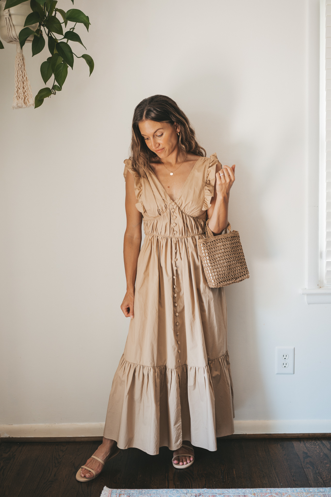 ashley wearing a tan midi dress with fabric buttons, nude sandals, and a woven bag