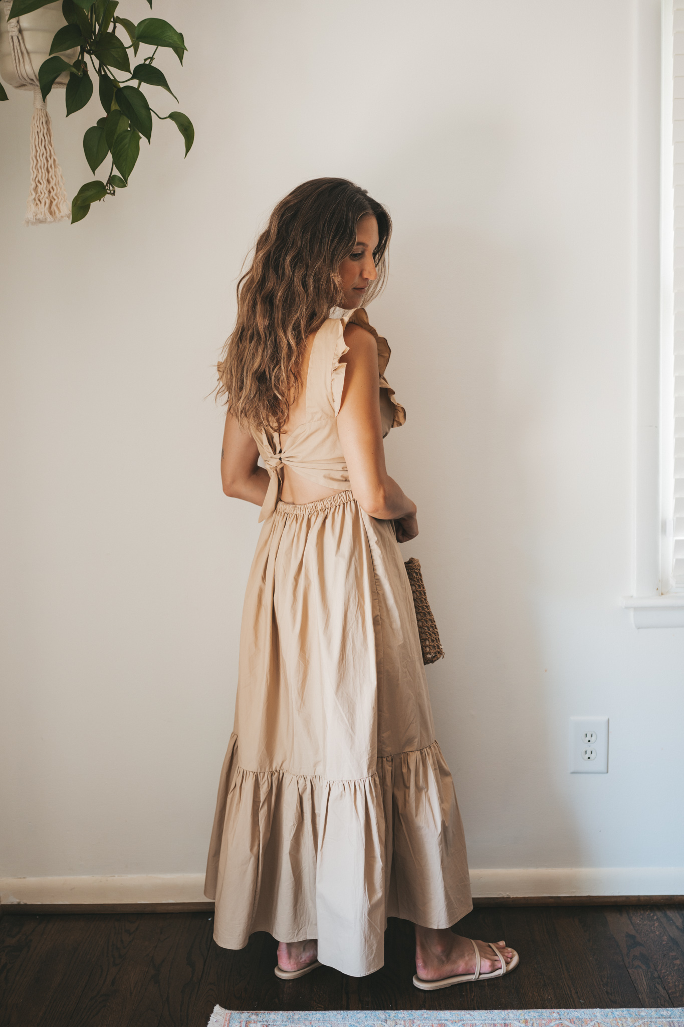ashley wearing a tan midi dress with fabric buttons, nude sandals, and a woven bag