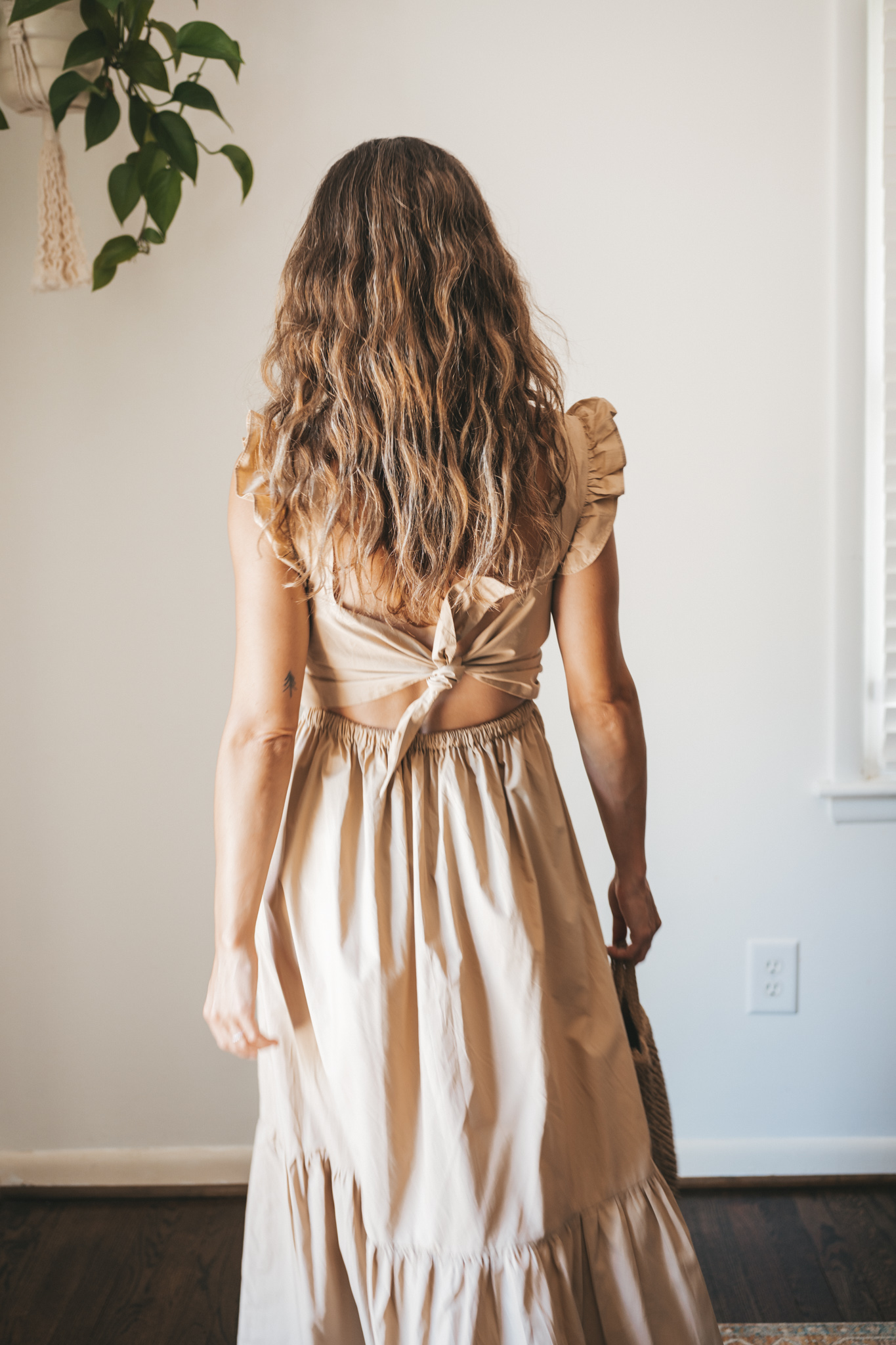 ashley wearing a tan midi dress with fabric buttons, nude sandals, and a woven bag