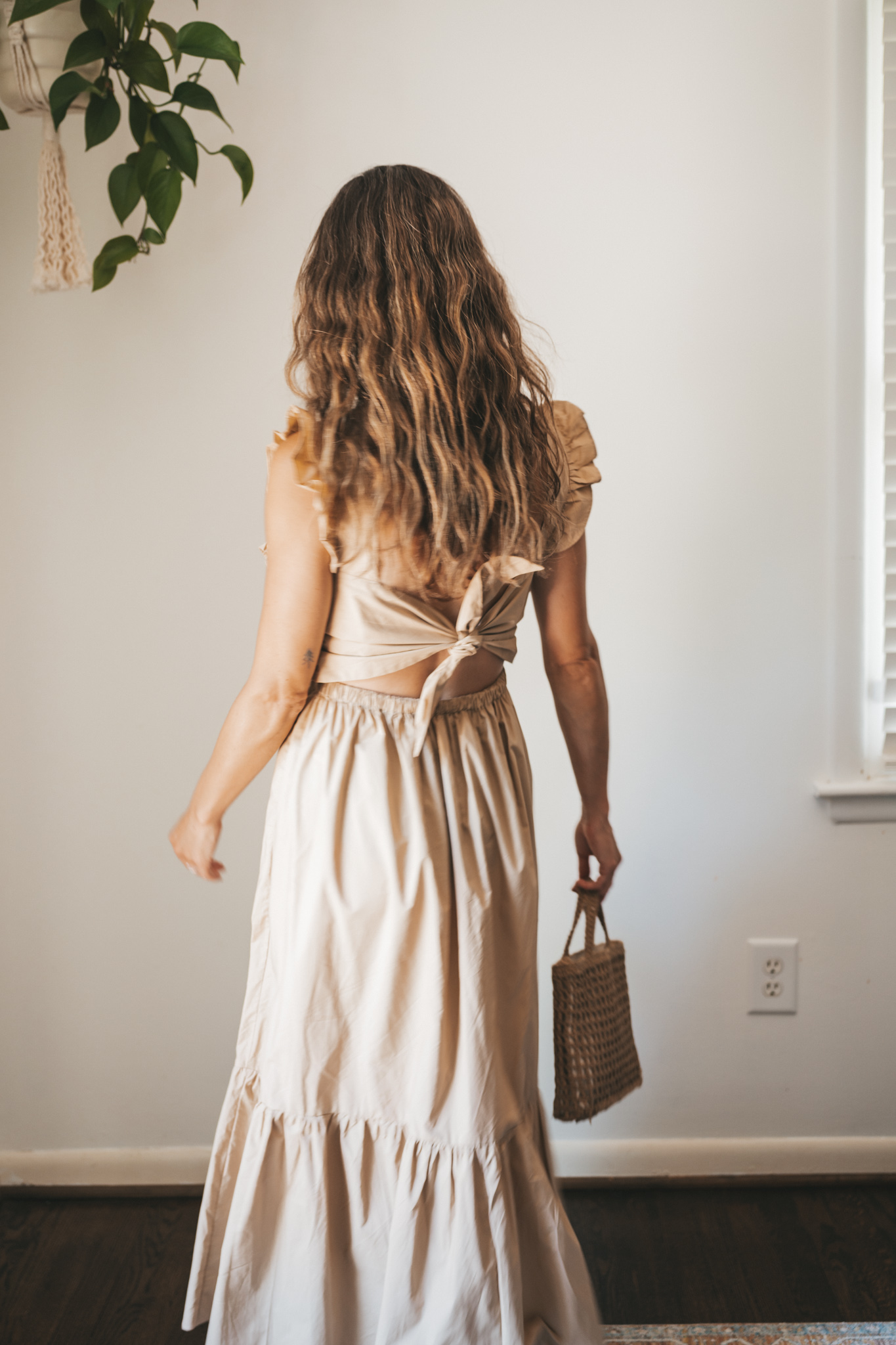 ashley wearing a tan midi dress with fabric buttons, nude sandals, and a woven bag