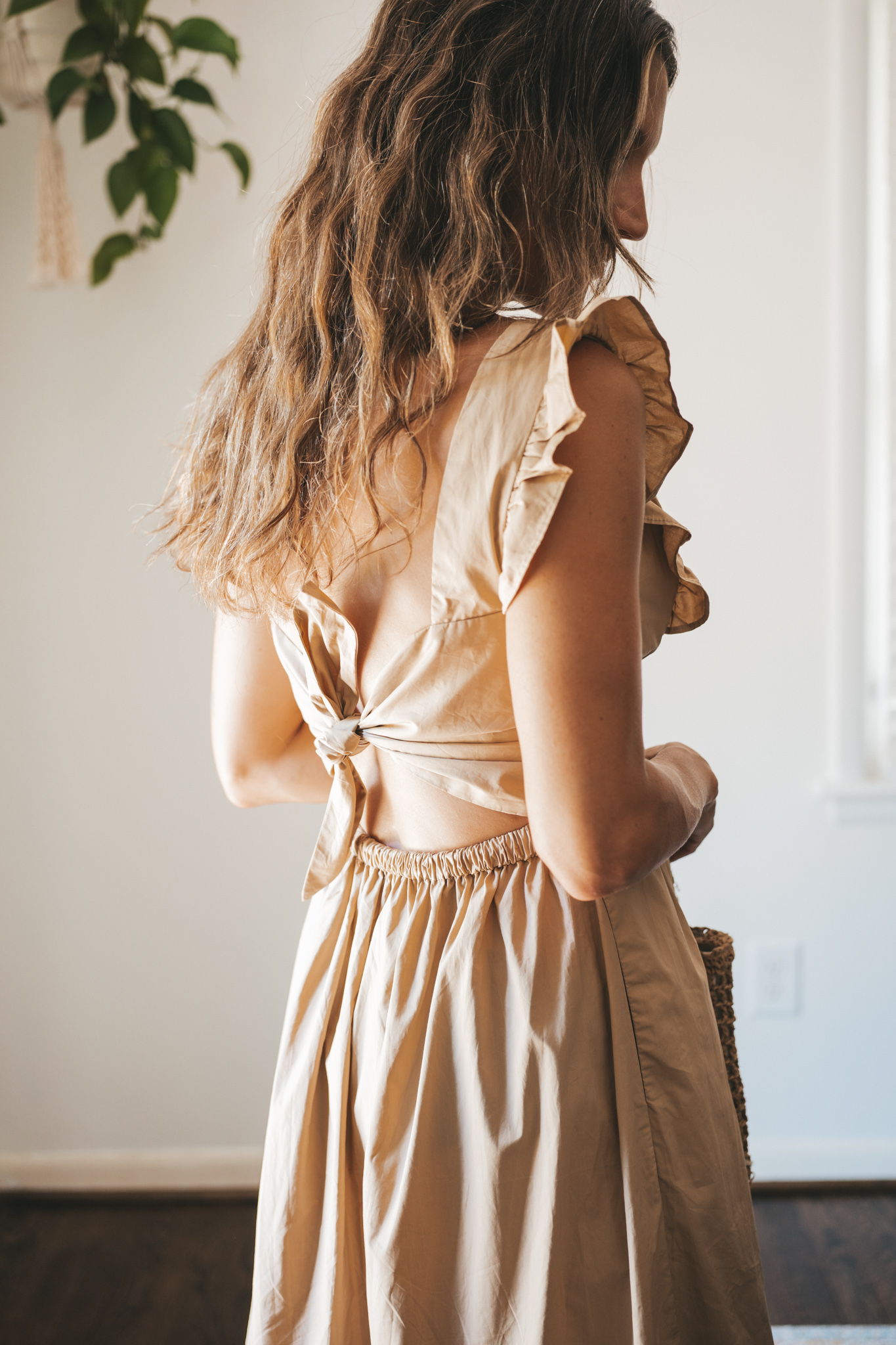 ashley wearing a tan midi dress with fabric buttons, nude sandals, and a woven bag