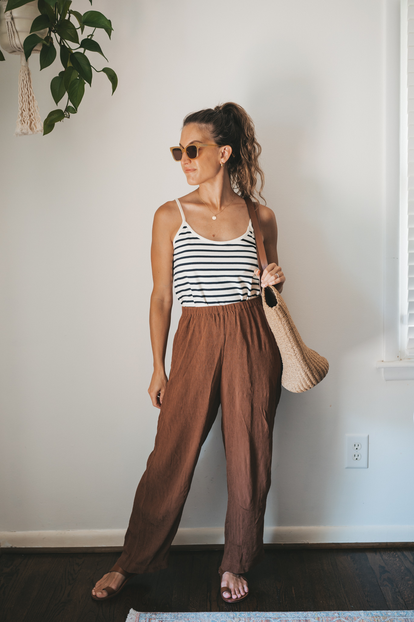 ashley wearing a white and navy striped tank, chocolate brown tapered loose pants, brown leather sandals, and a woven tote bag