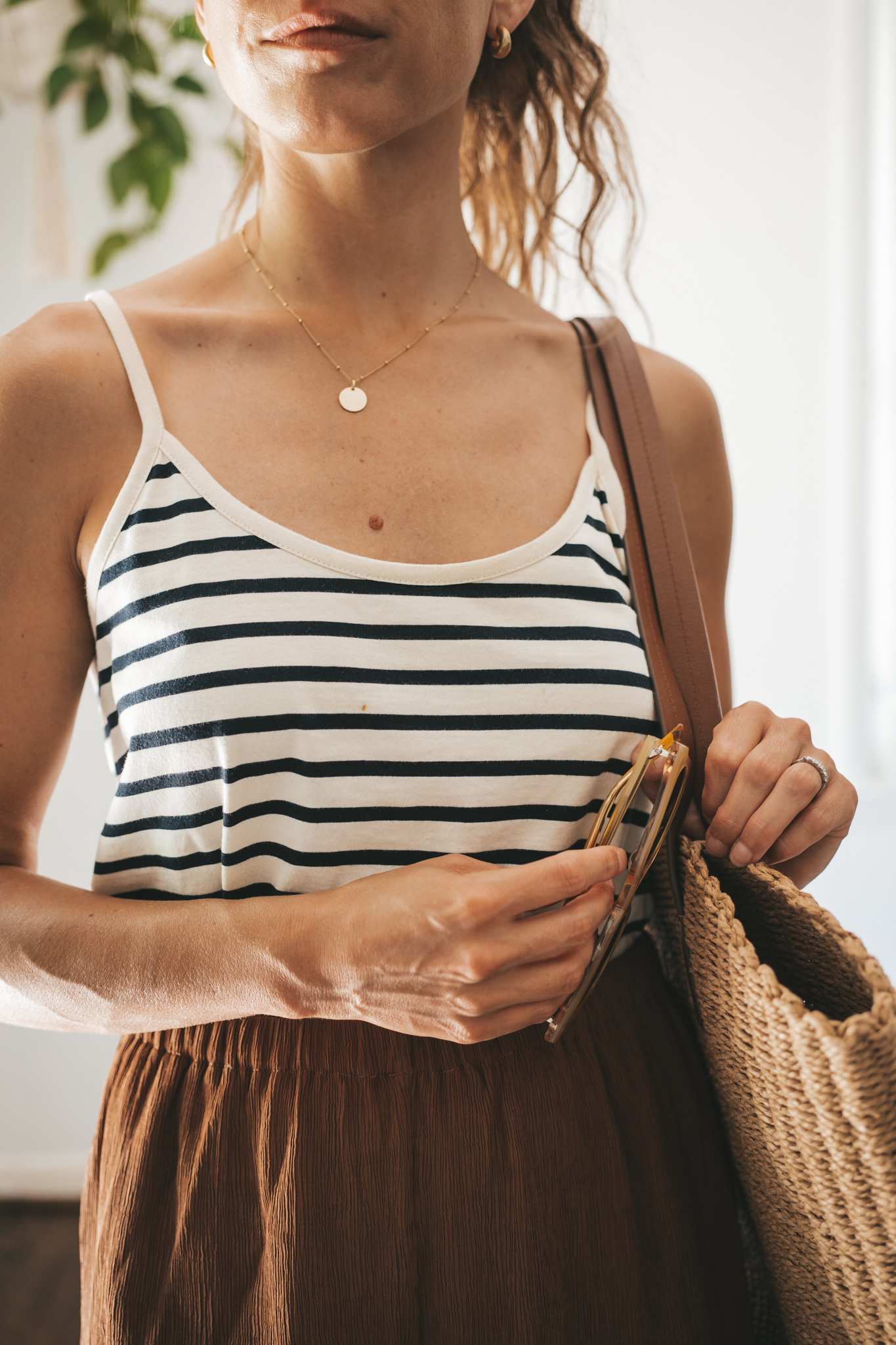 ashley wearing a white and navy striped tank, chocolate brown tapered loose pants, brown leather sandals, and a woven tote bag