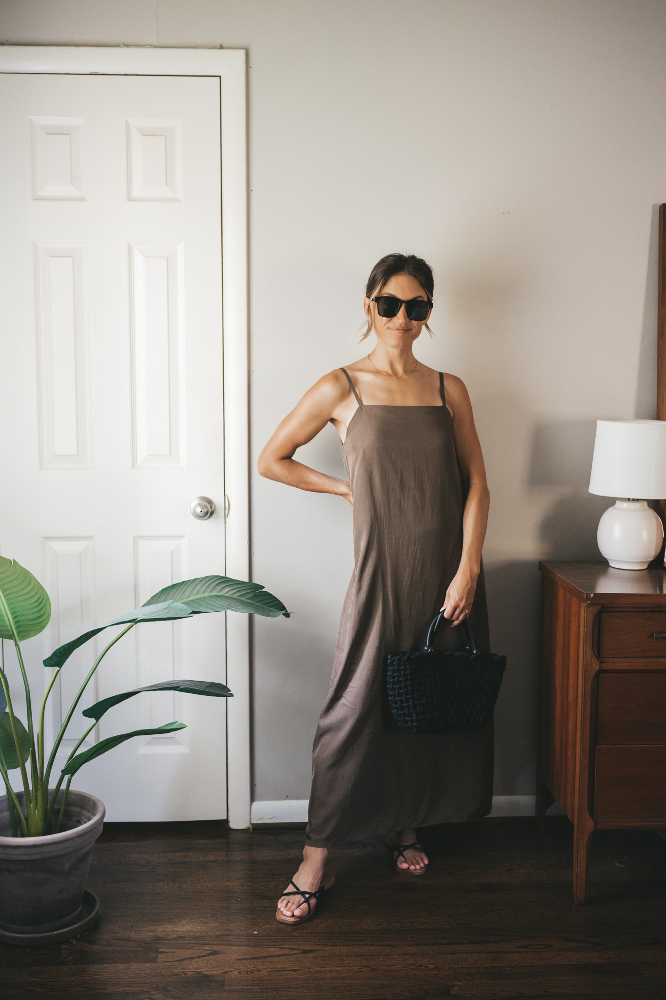 ashley wearing a green slip dress, black woven bag, black strappy sandals, and tortoise shell sunglasses