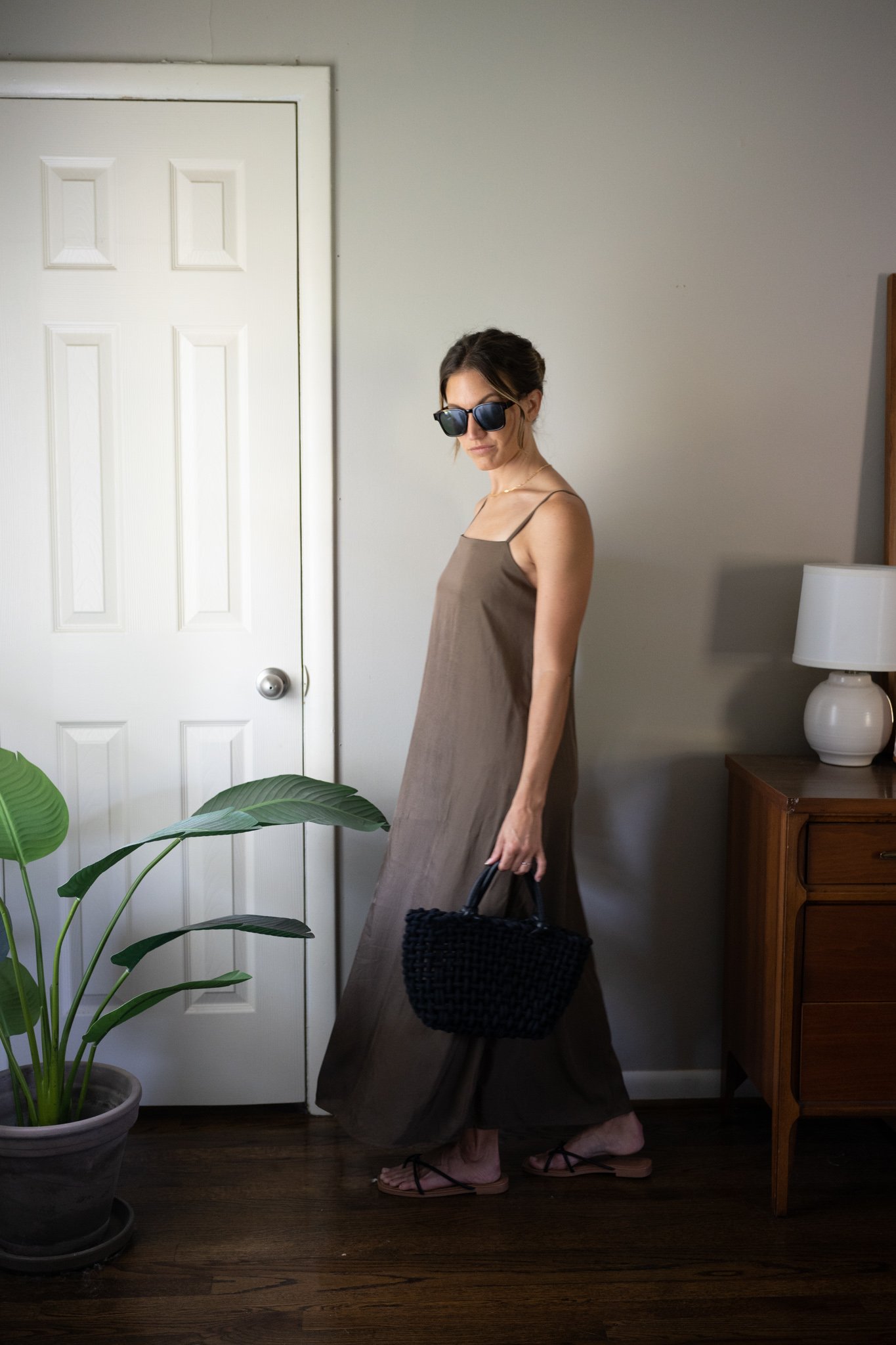 ashley wearing a green slip dress, black woven bag, black strappy sandals, and tortoise shell sunglasses