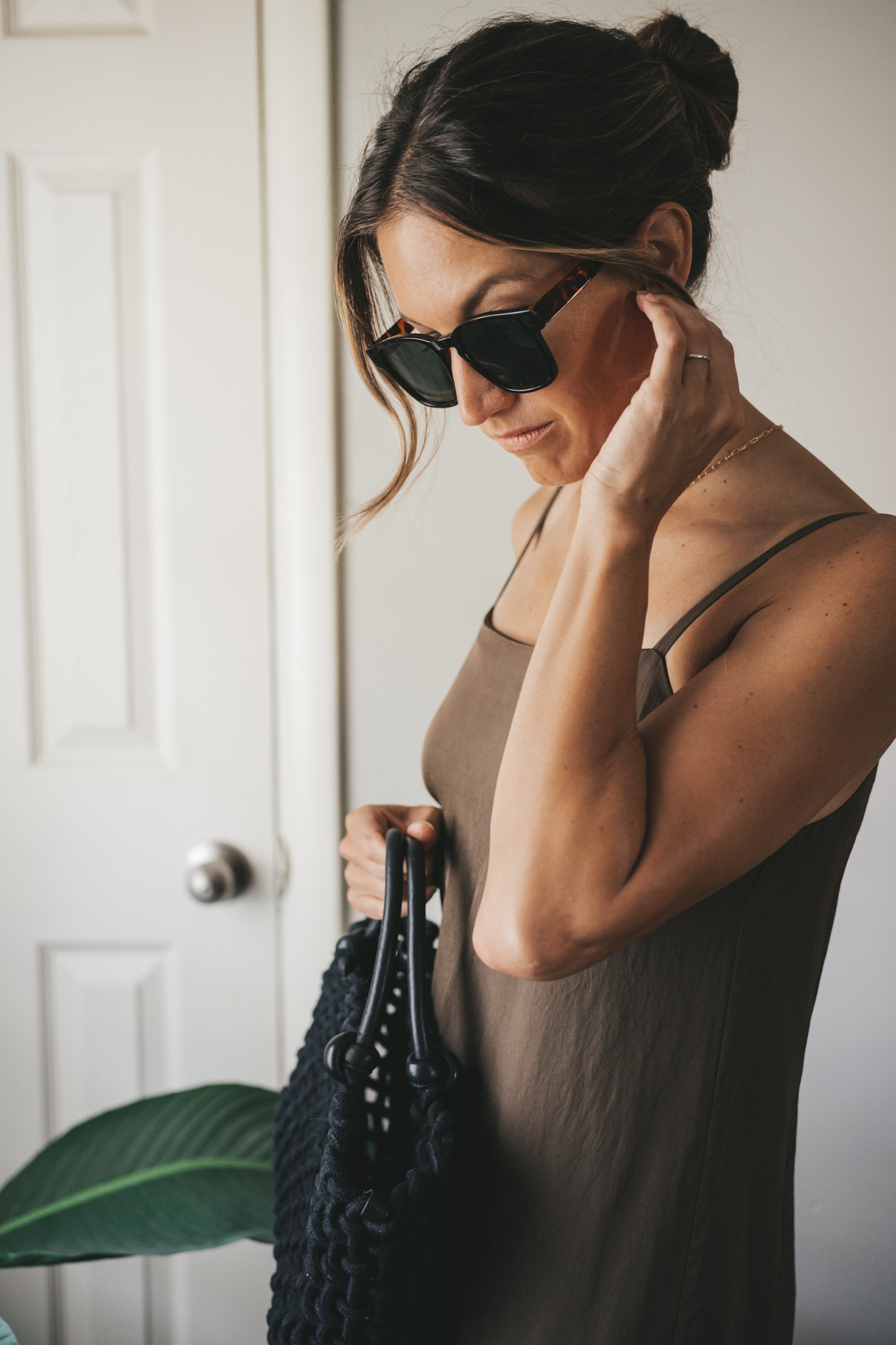 ashley wearing a green slip dress, black woven bag, black strappy sandals, and tortoise shell sunglasses