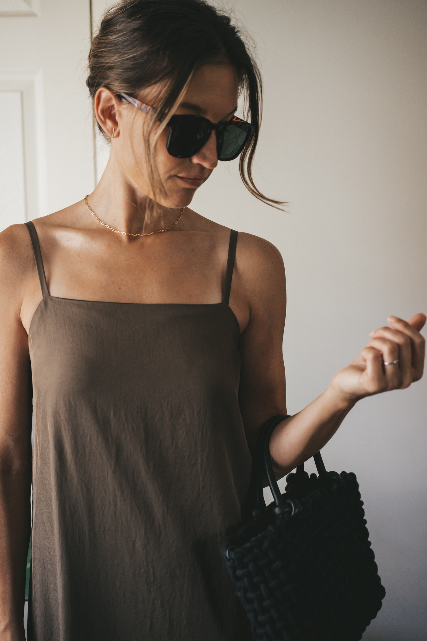 ashley wearing a green slip dress, black woven bag, black strappy sandals, and tortoise shell sunglasses