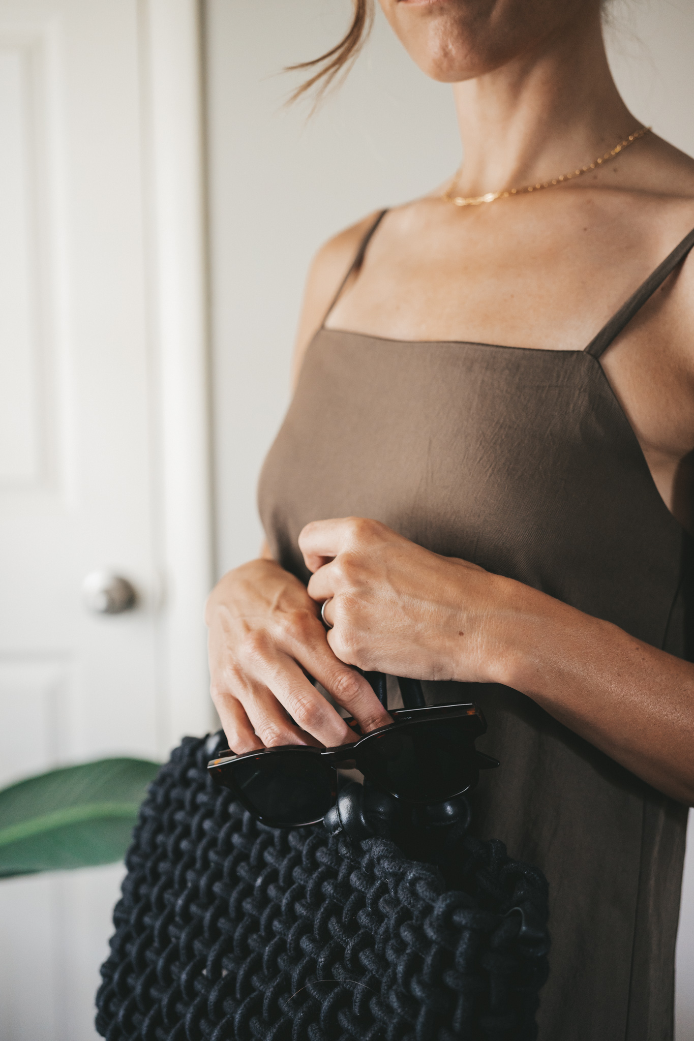 ashley wearing a green slip dress, black woven bag, black strappy sandals, and tortoise shell sunglasses