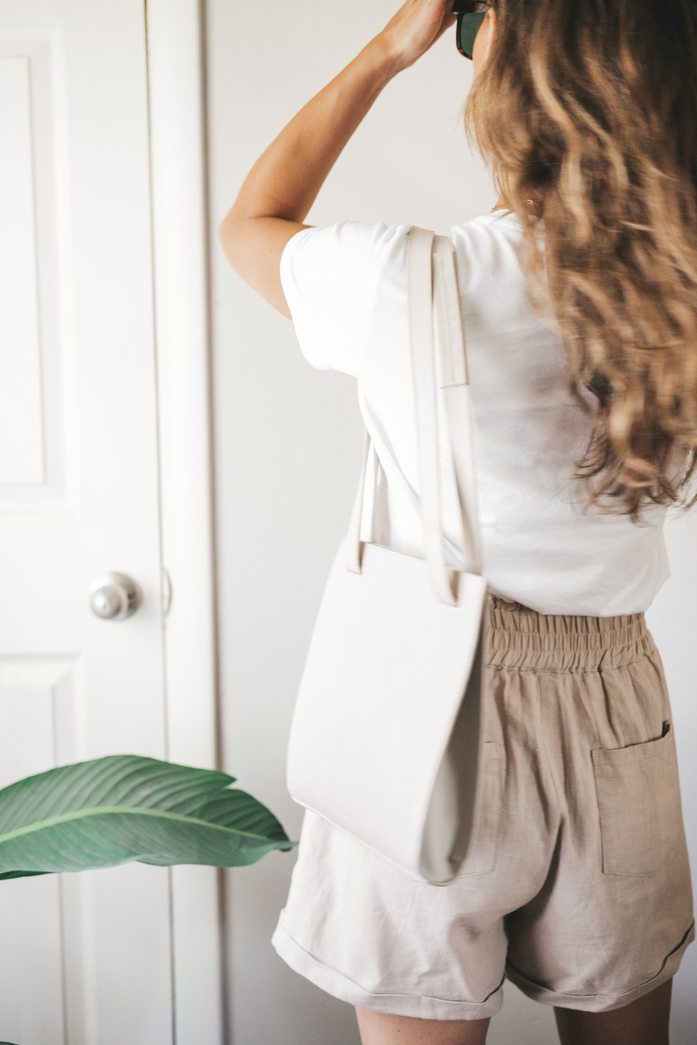 ashley wearing a white tee, tan linen shorts, white sandals, a gray shoulder bag, and tortoise shell sunglasses