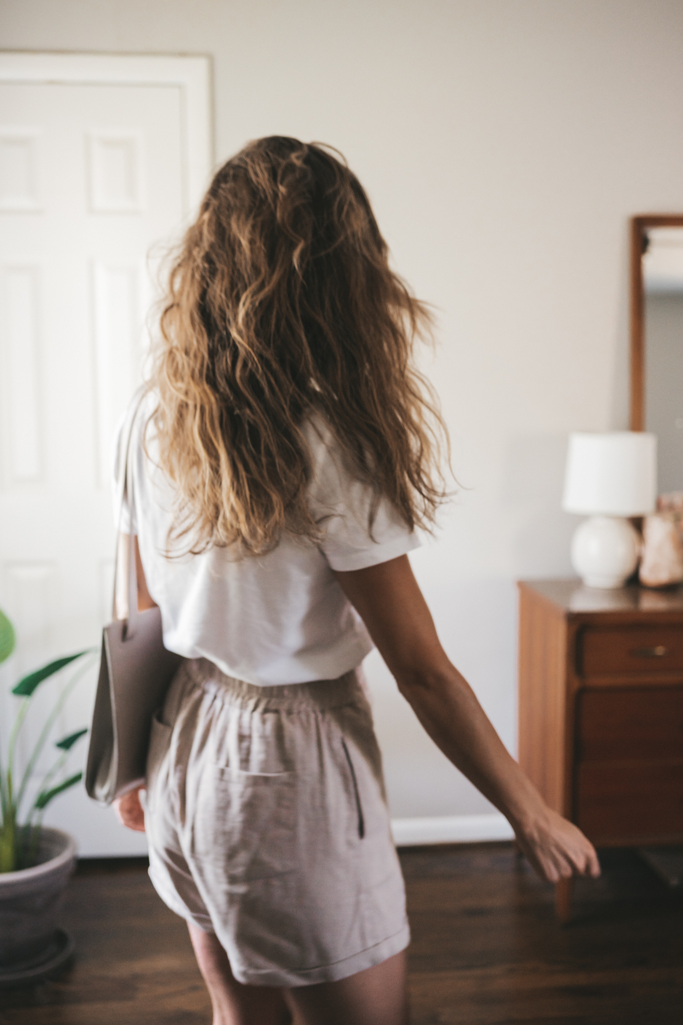 ashley wearing a white tee, tan linen shorts, white sandals, a gray shoulder bag, and tortoise shell sunglasses