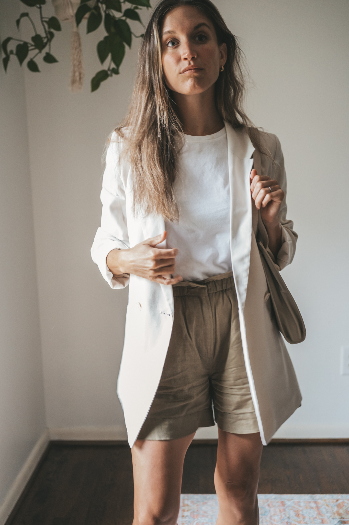 ashley wearing a white tee, beige oversized blazer, olive green paperbag shorts, white sneakers, and a gray shoulder bag