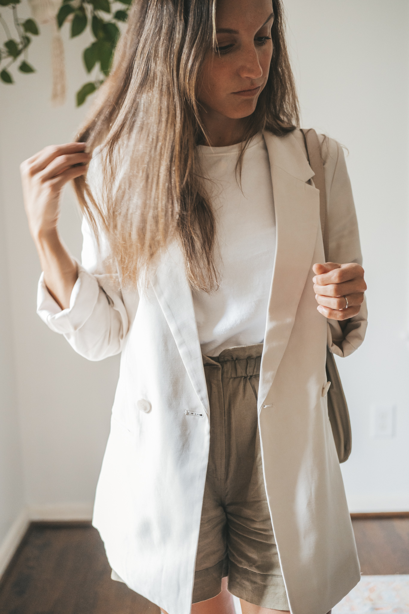 ashley wearing a white tee, beige oversized blazer, olive green paperbag shorts, white sneakers, and a gray shoulder bag