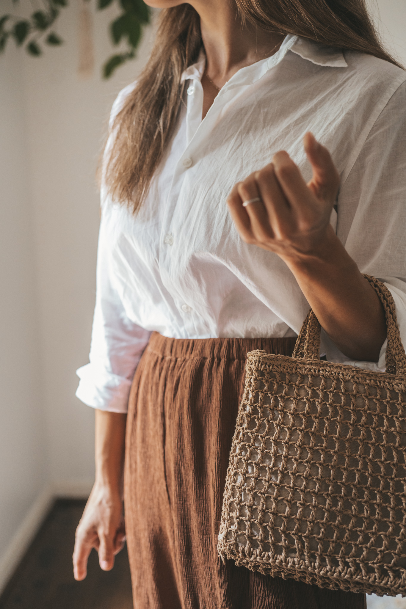 ashley wearing a white button down, brown drapey pants, brown leather sandals, and a woven bag