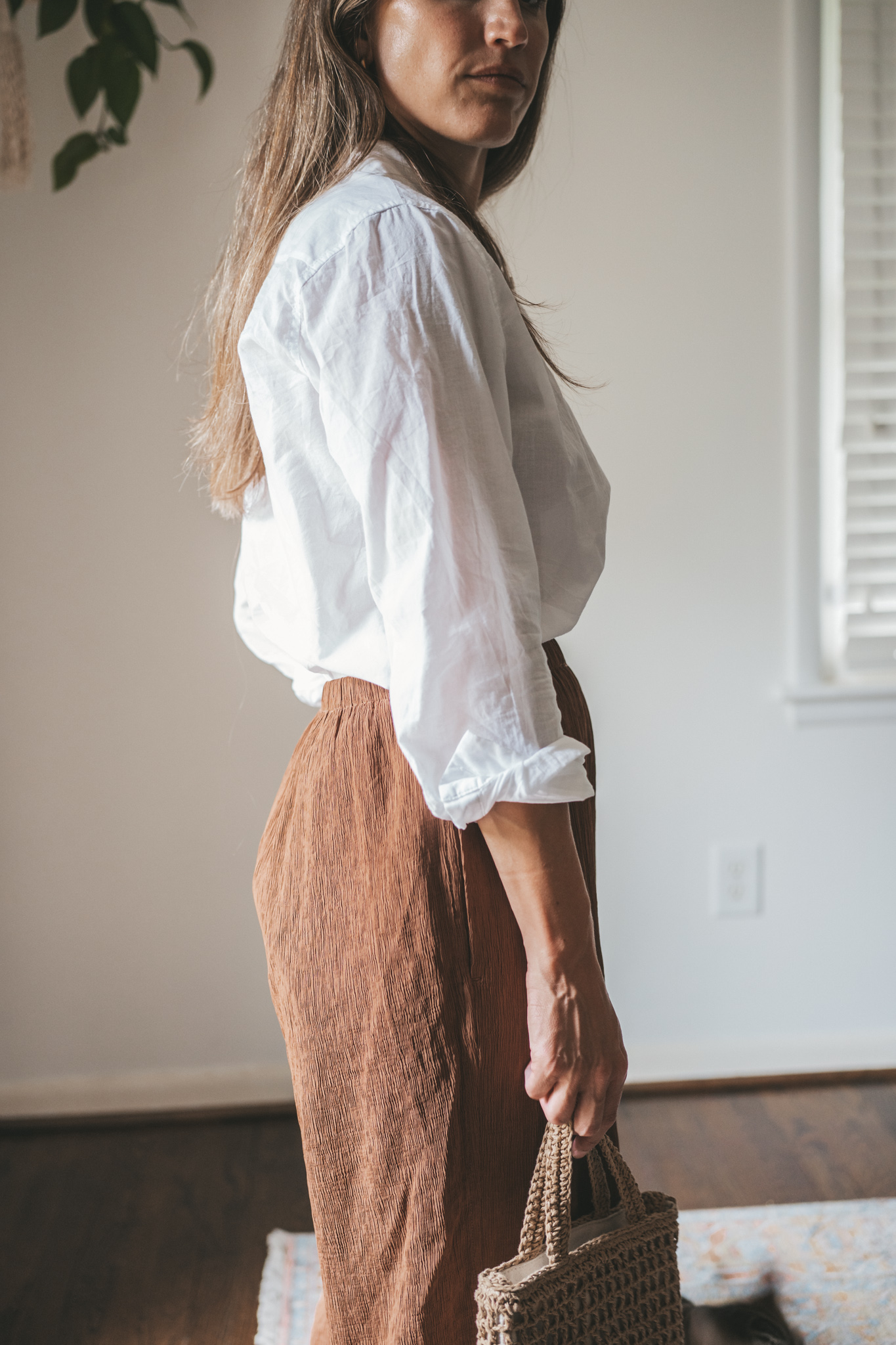 ashley wearing a white button down, brown drapey pants, brown leather sandals, and a woven bag
