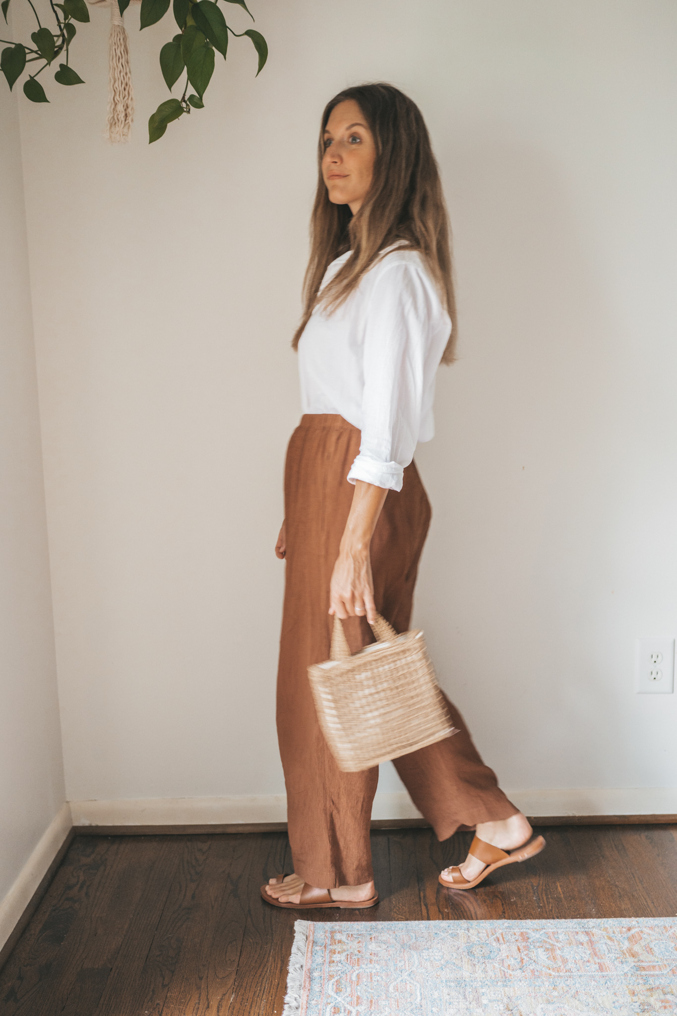 ashley wearing a white button down, brown drapey pants, brown leather sandals, and a woven bag