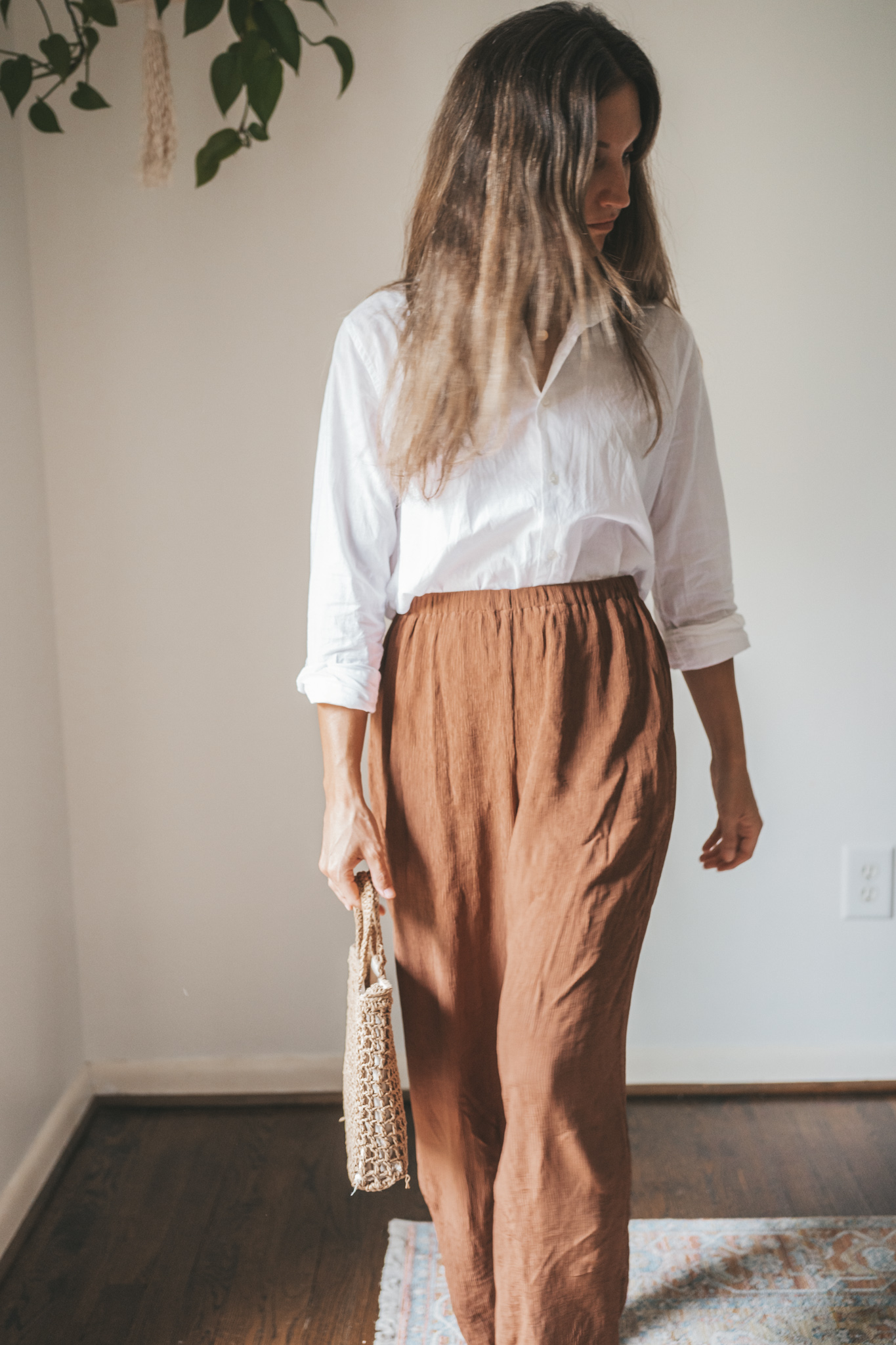 ashley wearing a white button down, brown drapey pants, brown leather sandals, and a woven bag