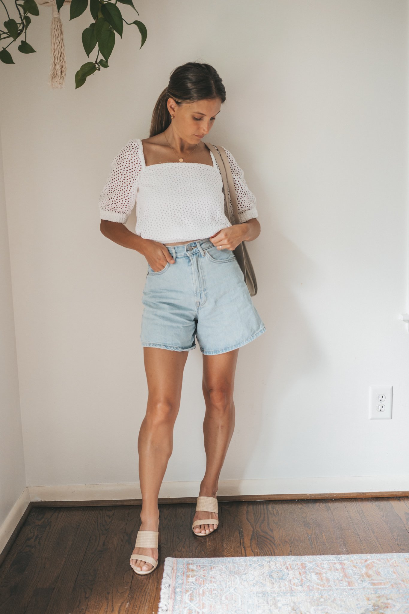 ashley wearing a puff sleeve eyelet top, light wash a-line denim shorts, woven heeled sandals, and a gray shoulder bag
