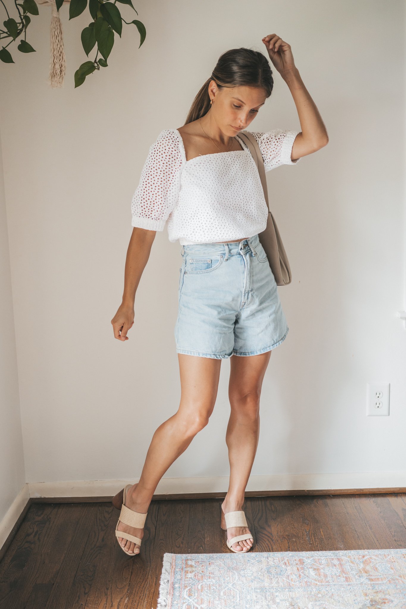 ashley wearing a puff sleeve eyelet top, light wash a-line denim shorts, woven heeled sandals, and a gray shoulder bag