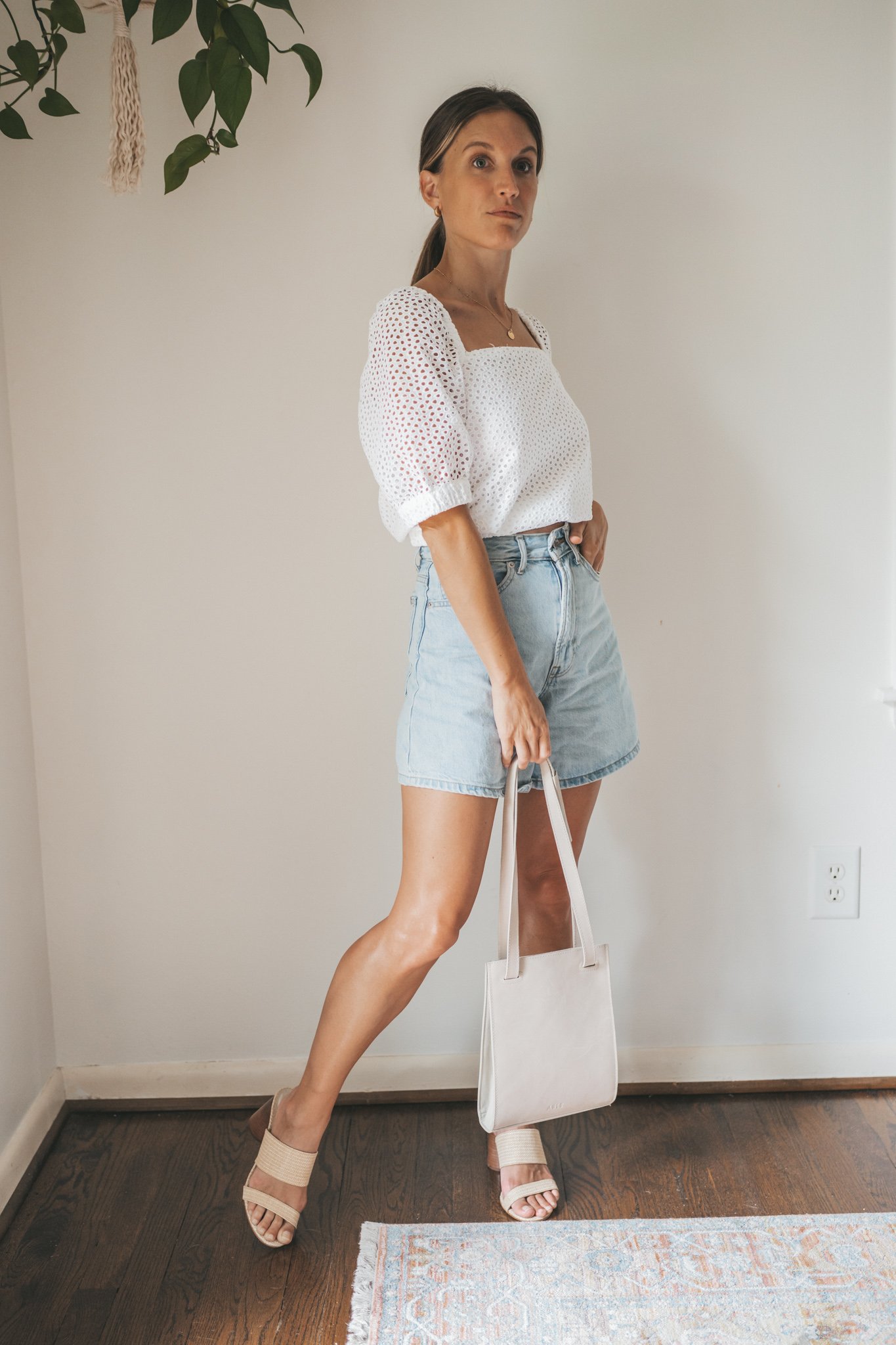 ashley wearing a puff sleeve eyelet top, light wash a-line denim shorts, woven heeled sandals, and a gray shoulder bag