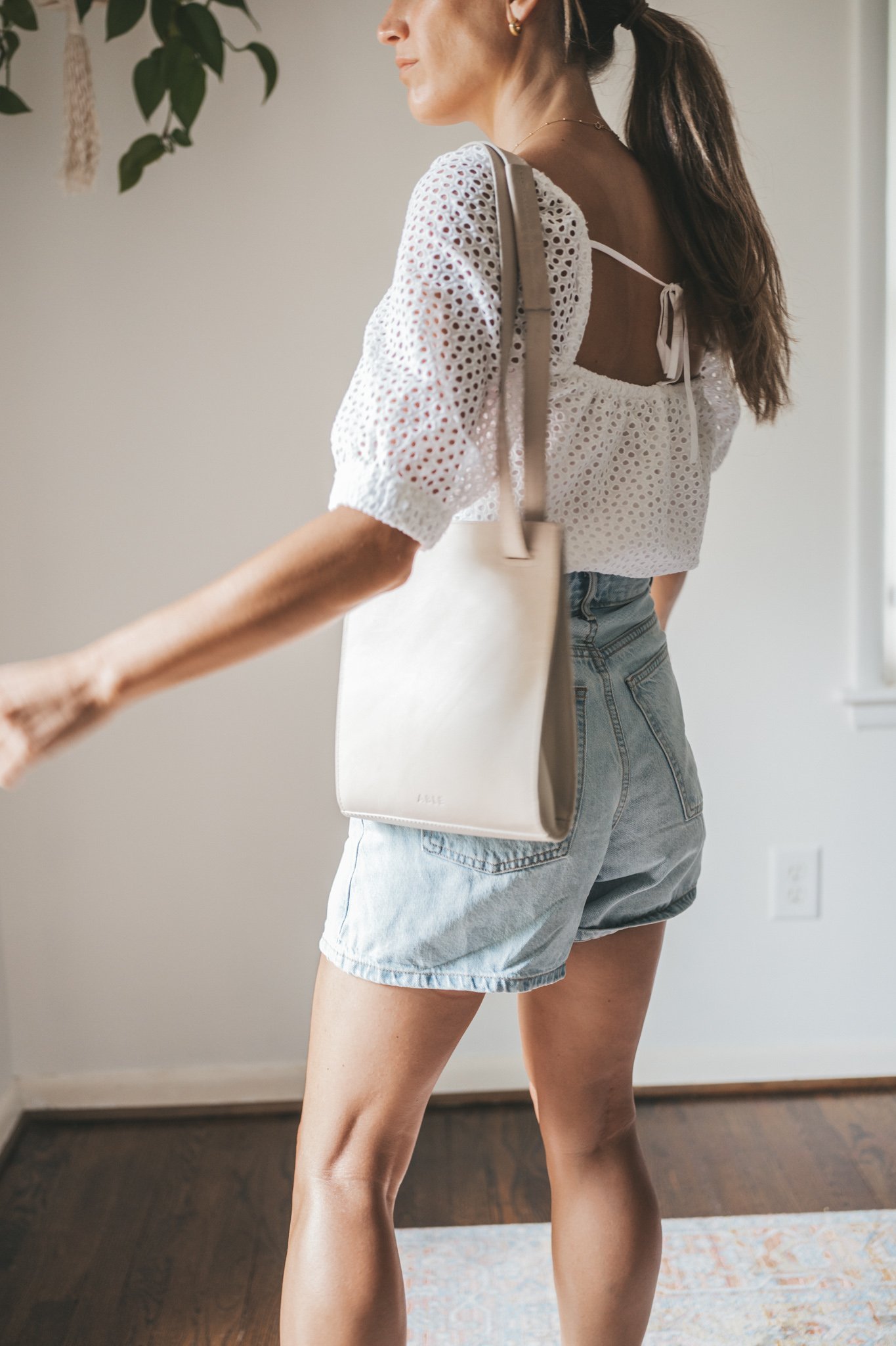 ashley wearing a puff sleeve eyelet top, light wash a-line denim shorts, woven heeled sandals, and a gray shoulder bag