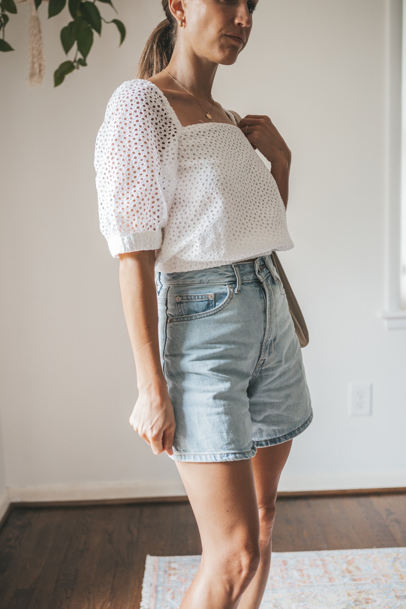 ashley wearing a puff sleeve eyelet top, light wash a-line denim shorts, woven heeled sandals, and a gray shoulder bag
