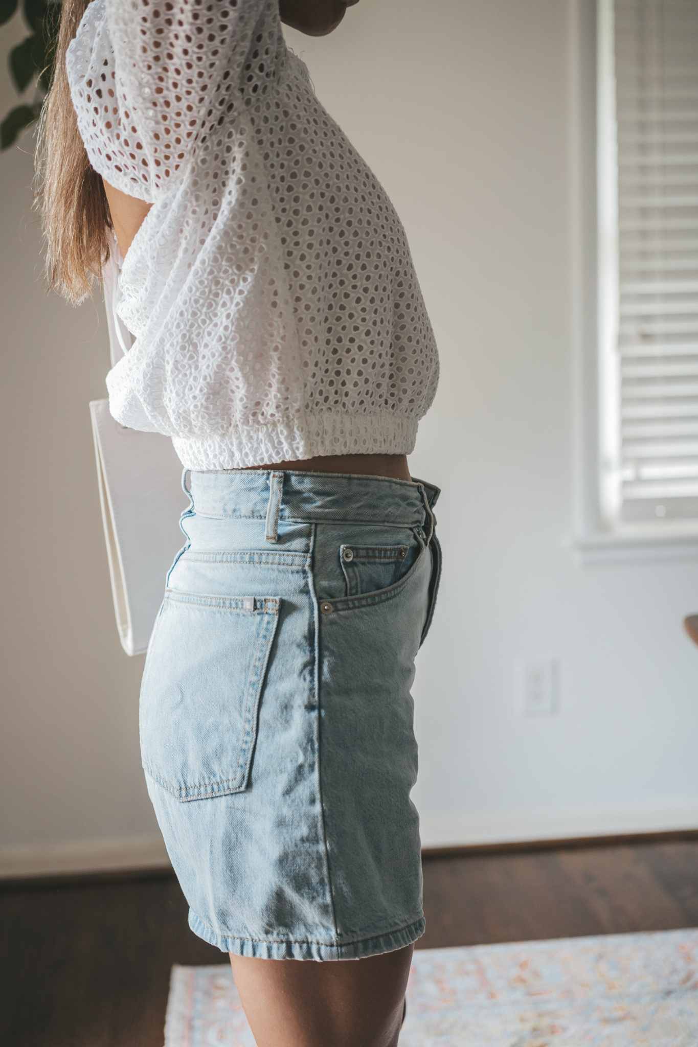 ashley wearing a puff sleeve eyelet top, light wash a-line denim shorts, woven heeled sandals, and a gray shoulder bag