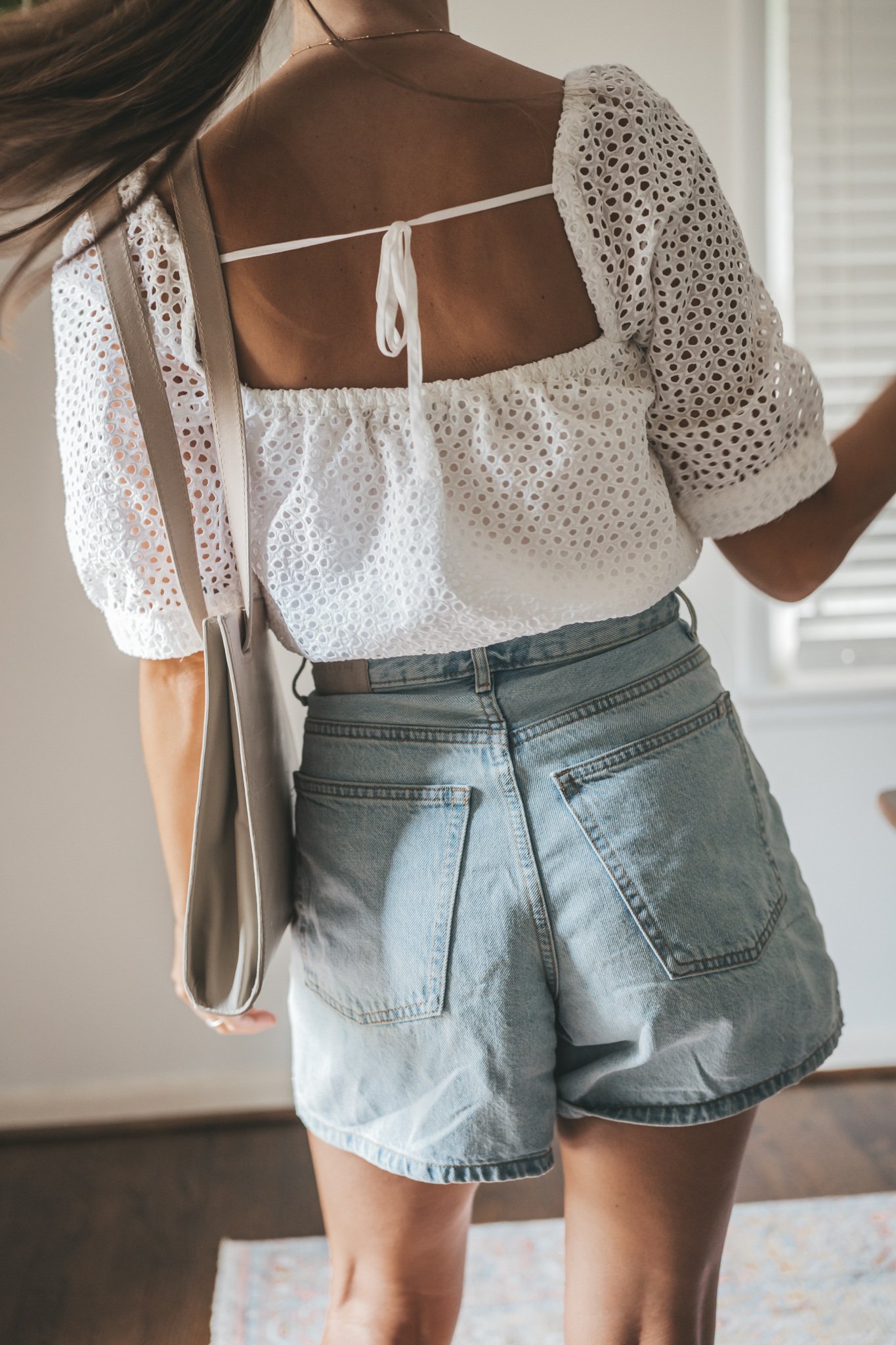 ashley wearing a puff sleeve eyelet top, light wash a-line denim shorts, woven heeled sandals, and a gray shoulder bag