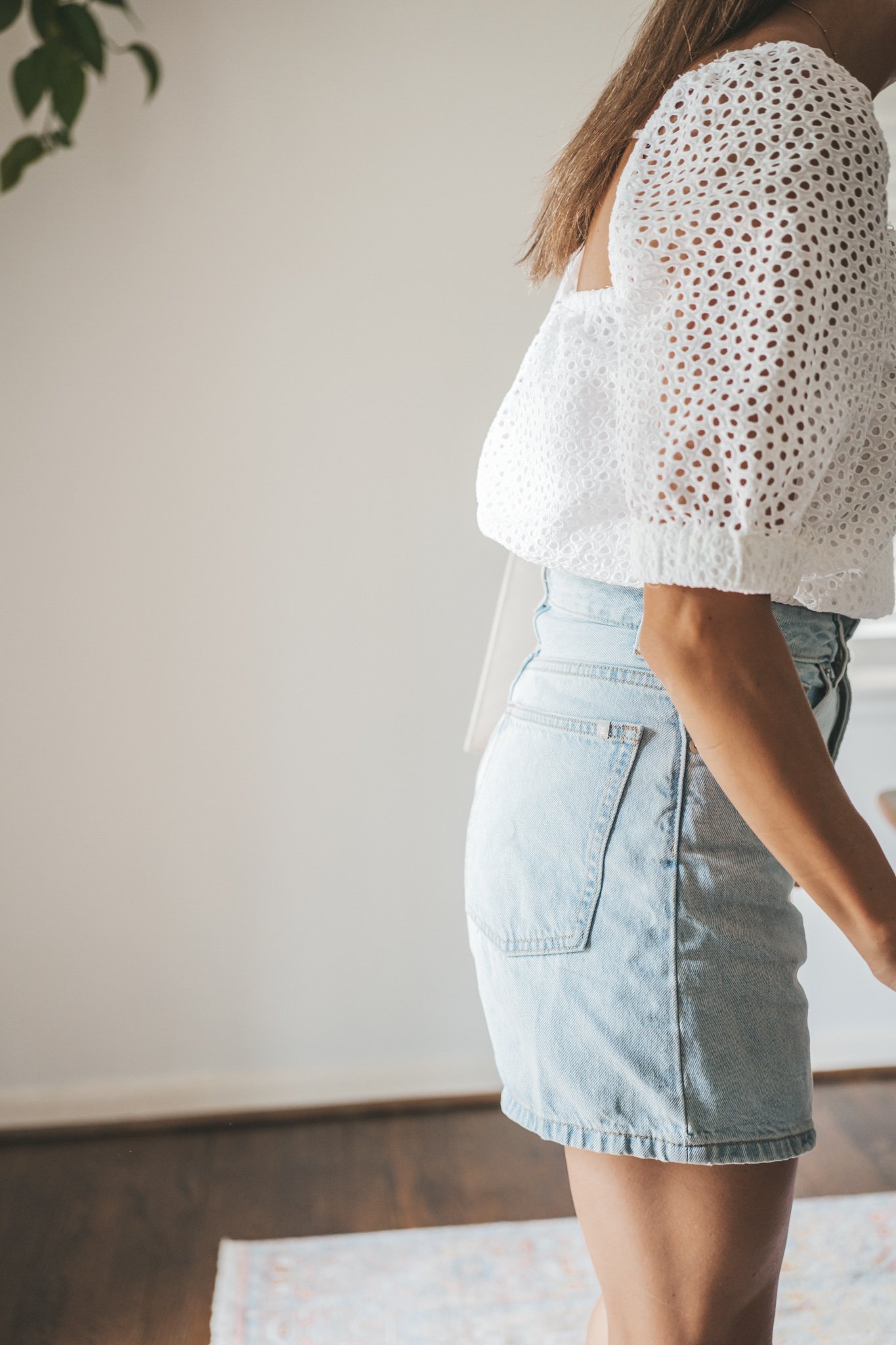 ashley wearing a puff sleeve eyelet top, light wash a-line denim shorts, woven heeled sandals, and a gray shoulder bag