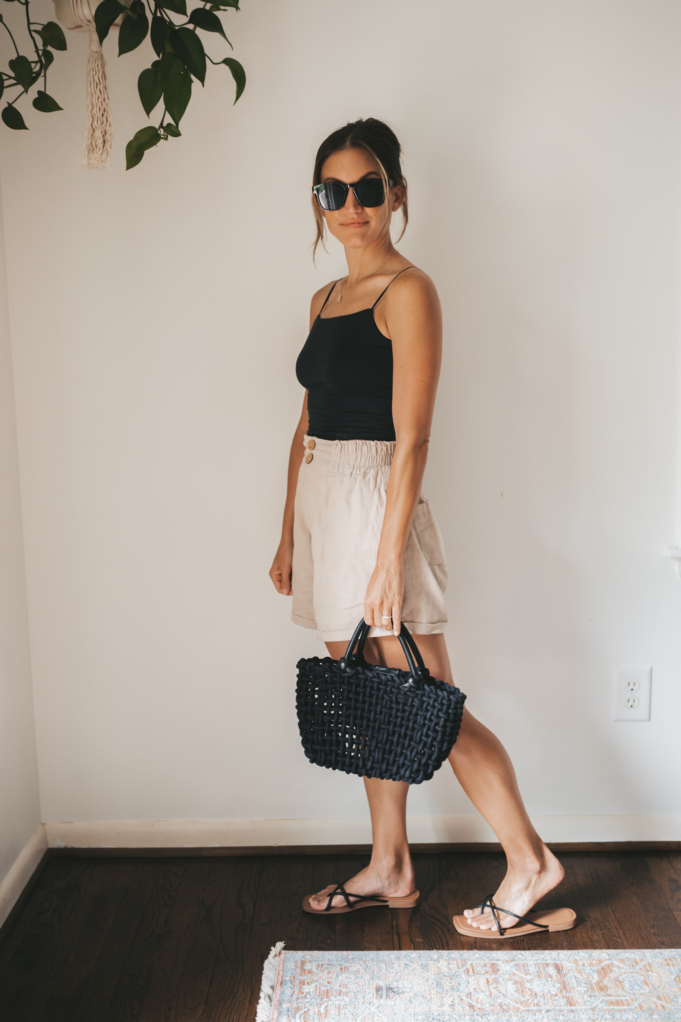 ashley wearing a black cropped tank, tan linen shorts, black strappy sandals, tortoise shell sunglasses and a black woven bag