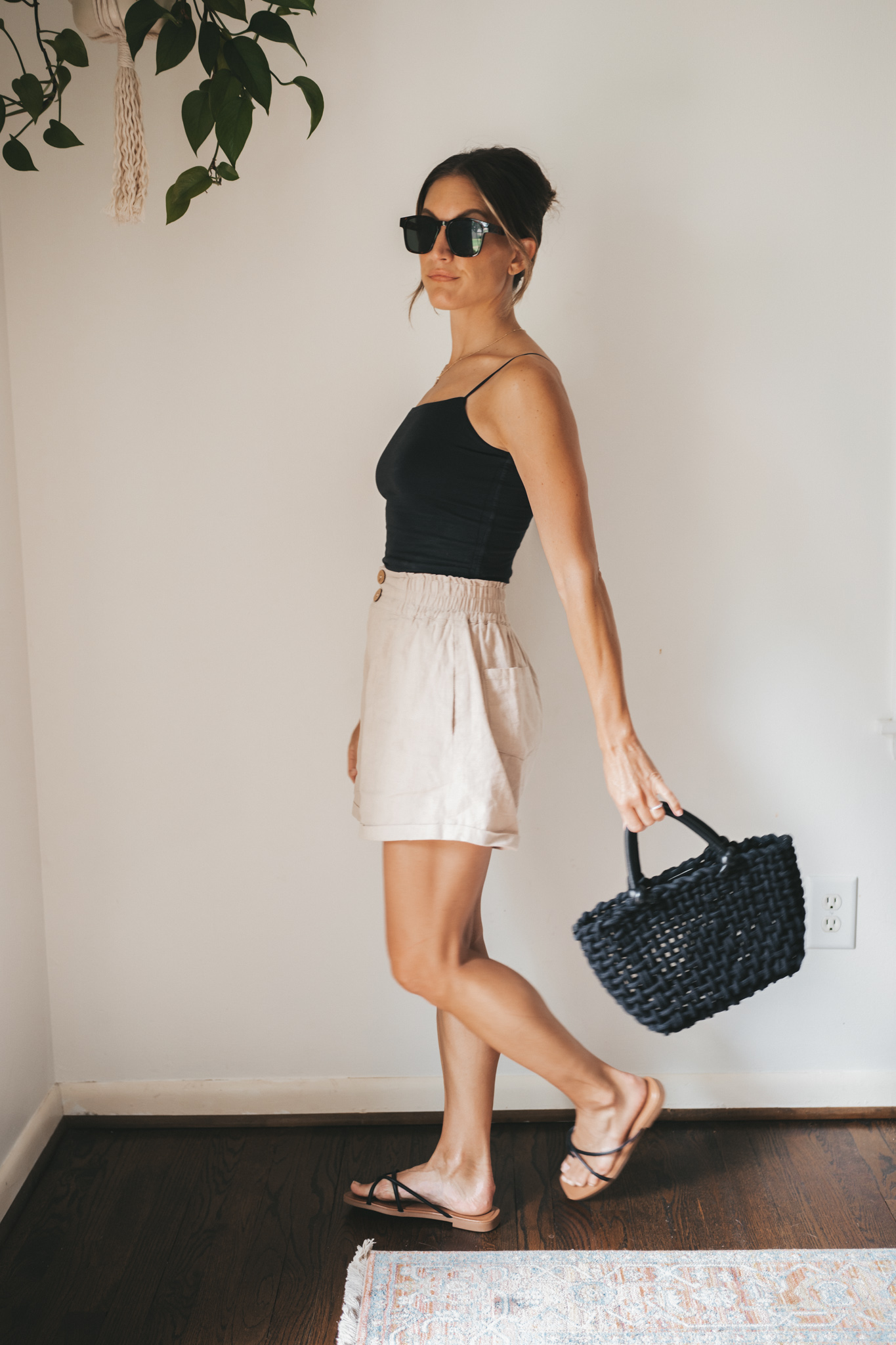 ashley wearing a black cropped tank, tan linen shorts, black strappy sandals, tortoise shell sunglasses and a black woven bag
