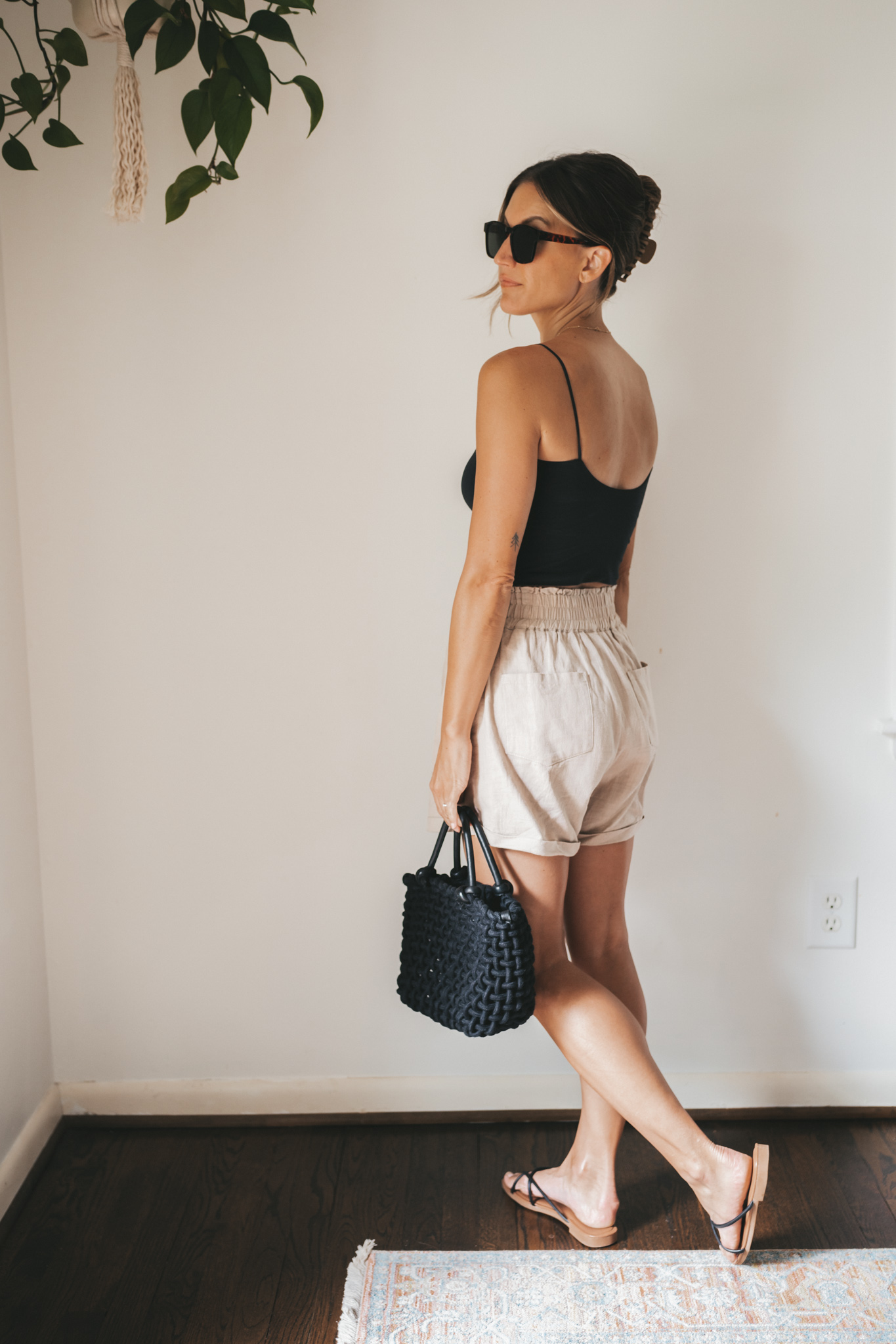 ashley wearing a black cropped tank, tan linen shorts, black strappy sandals, tortoise shell sunglasses and a black woven bag
