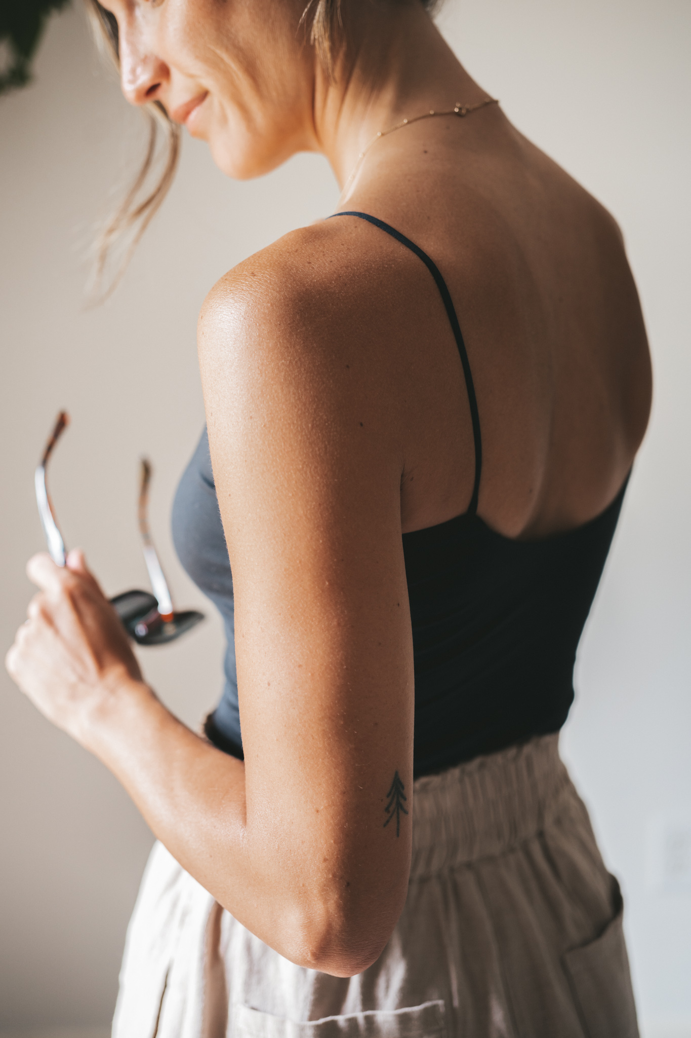 ashley wearing a black cropped tank, tan linen shorts, black strappy sandals, tortoise shell sunglasses and a black woven bag