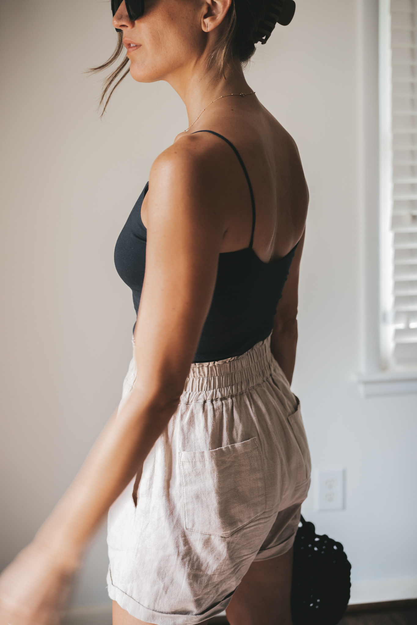 ashley wearing a black cropped tank, tan linen shorts, black strappy sandals, tortoise shell sunglasses and a black woven bag